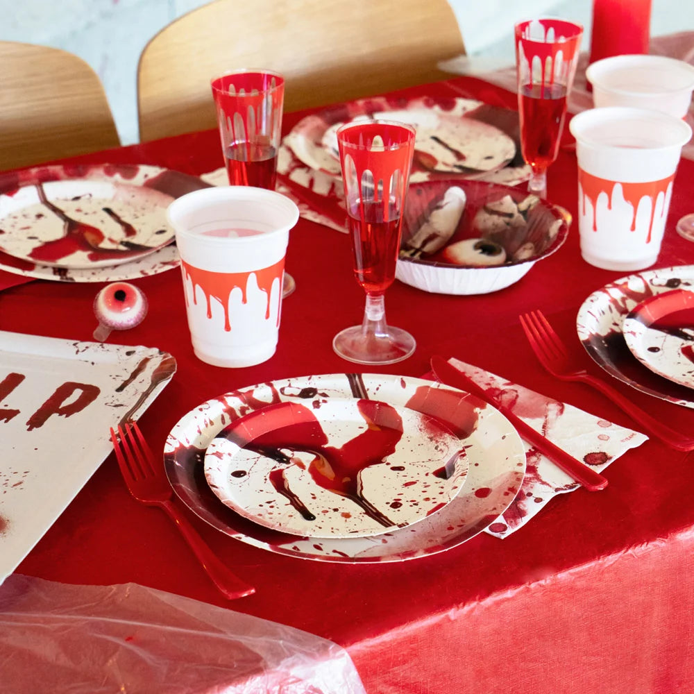 A red Halloween party table setting with blood-splatter plates, cups, and a white paper napkin featuring red blood smears.