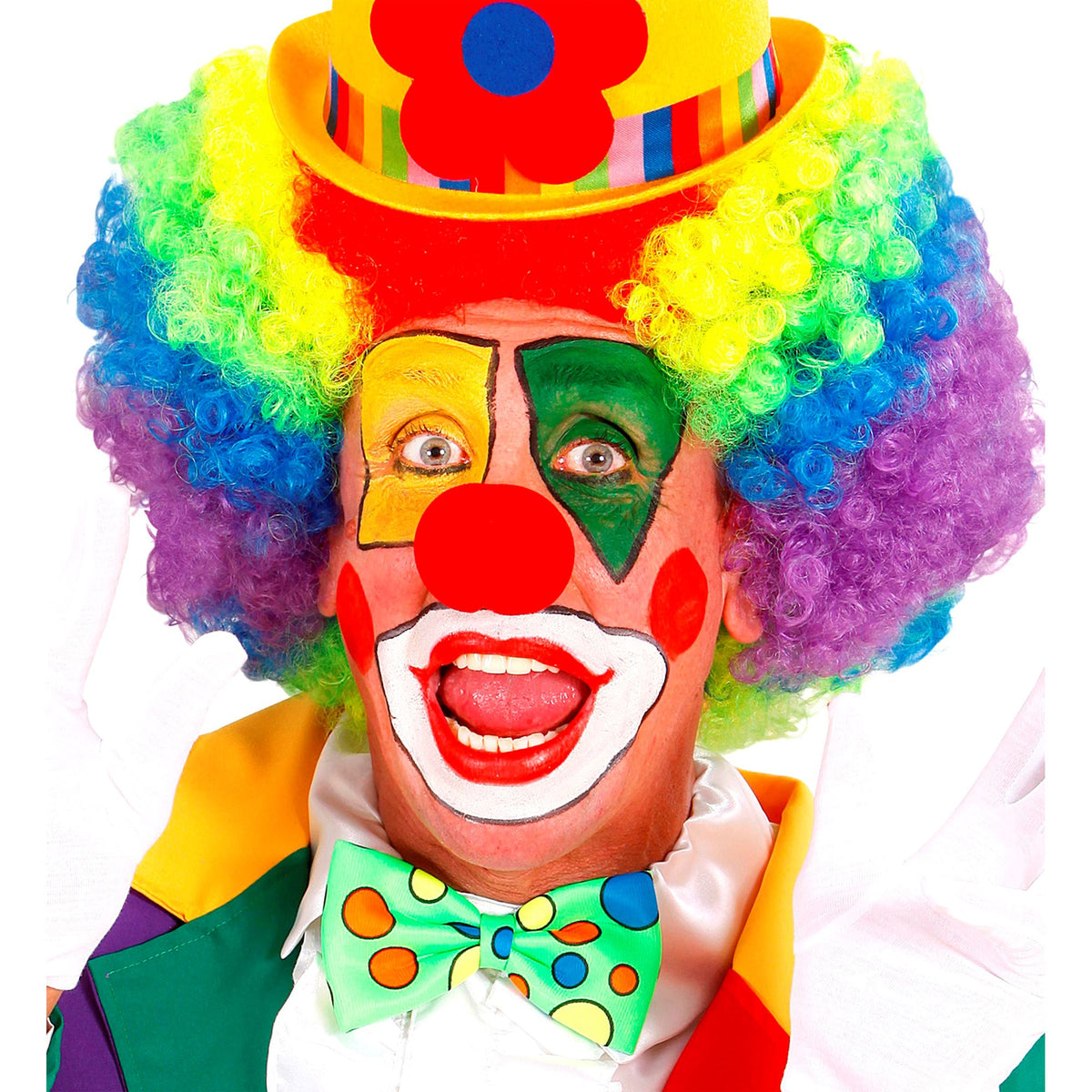 A close-up of a person wearing a bright rainbow clown wig, colorful clown makeup, a yellow hat with a red flower, and a green polka-dot bow tie against a white background.