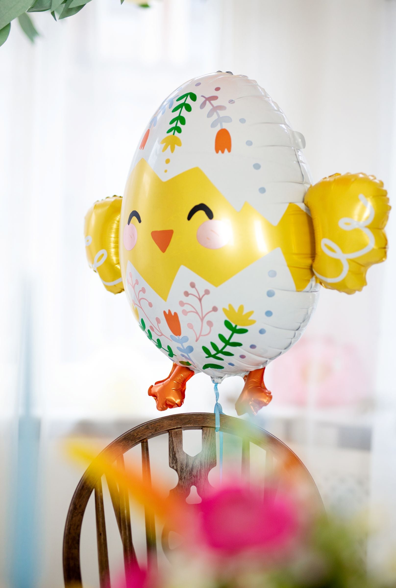 Detailed chick egg foil balloon floating above a chair highlighting the metallic gold finish.