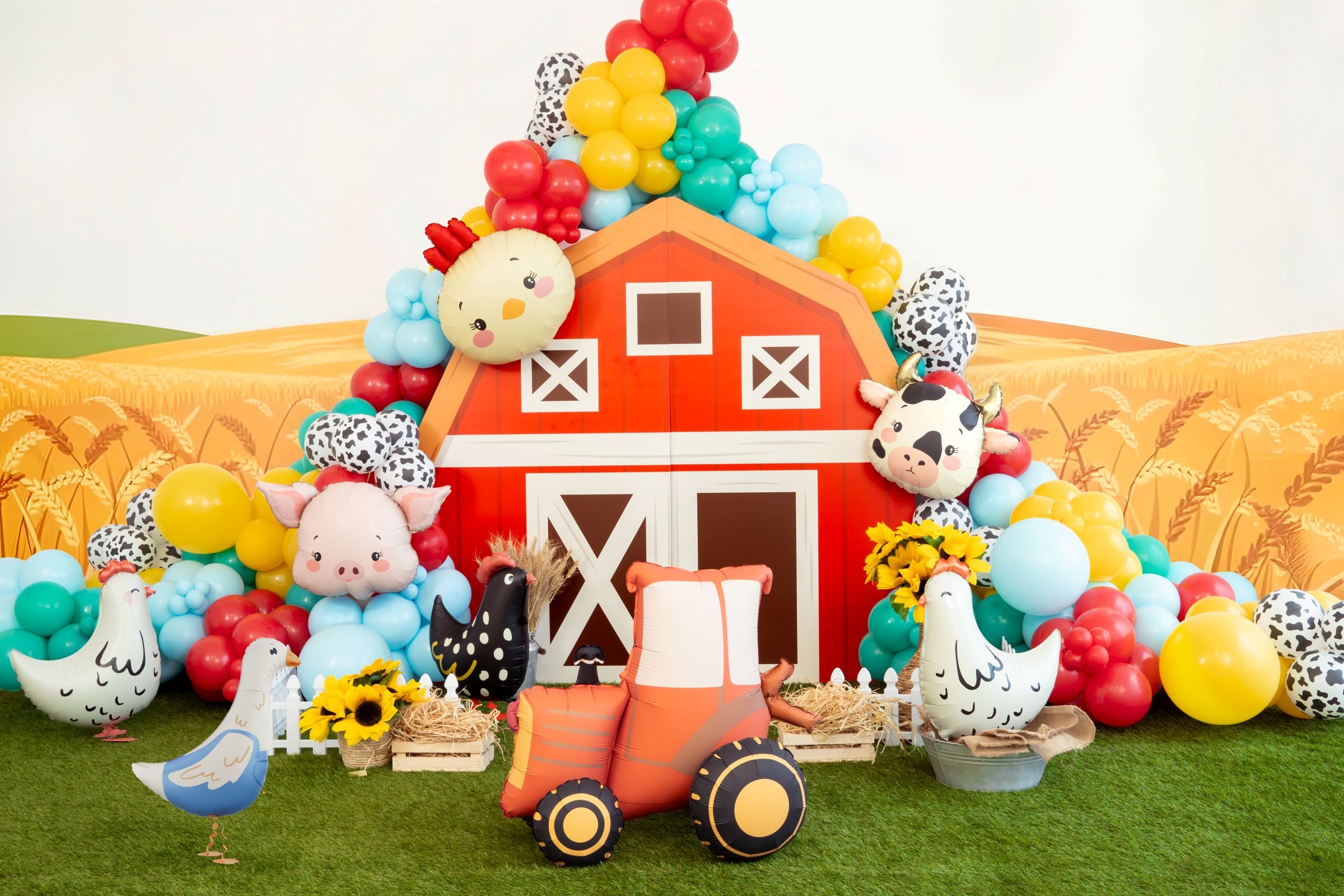 A festive farm-themed party backdrop featuring a red barn, colorful balloon arch, and various animal balloons including a yellow chicken, pig, and cow.