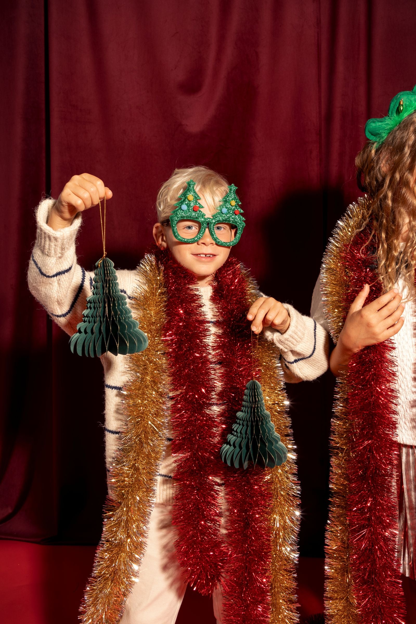 A child wearing the festive green Christmas tree glasses while holding a honeycomb Christmas decoration.