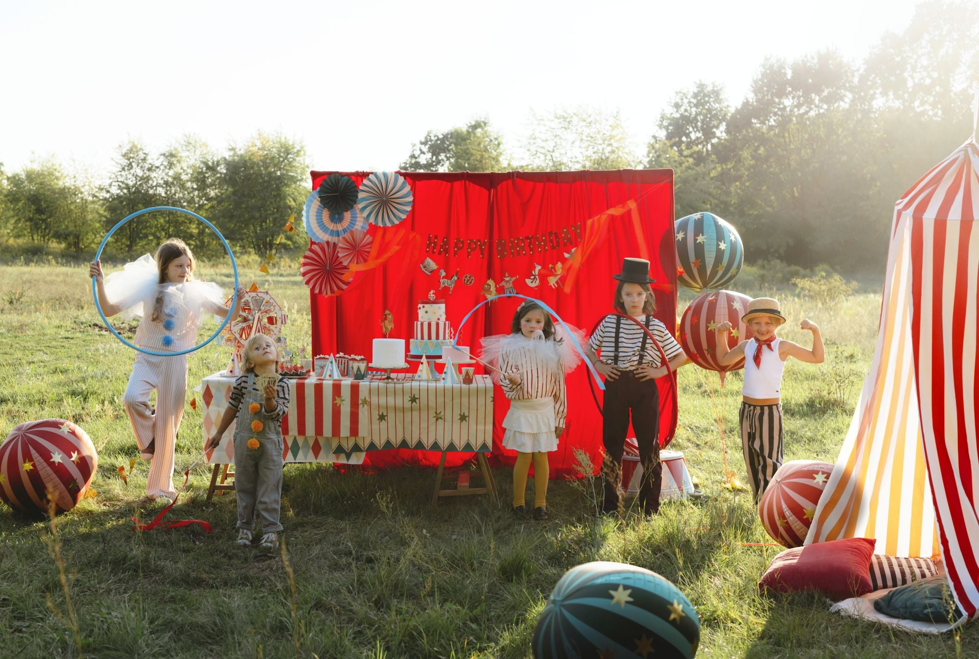 Children in a circus-themed outdoor setting with a red backdrop and striped tent.