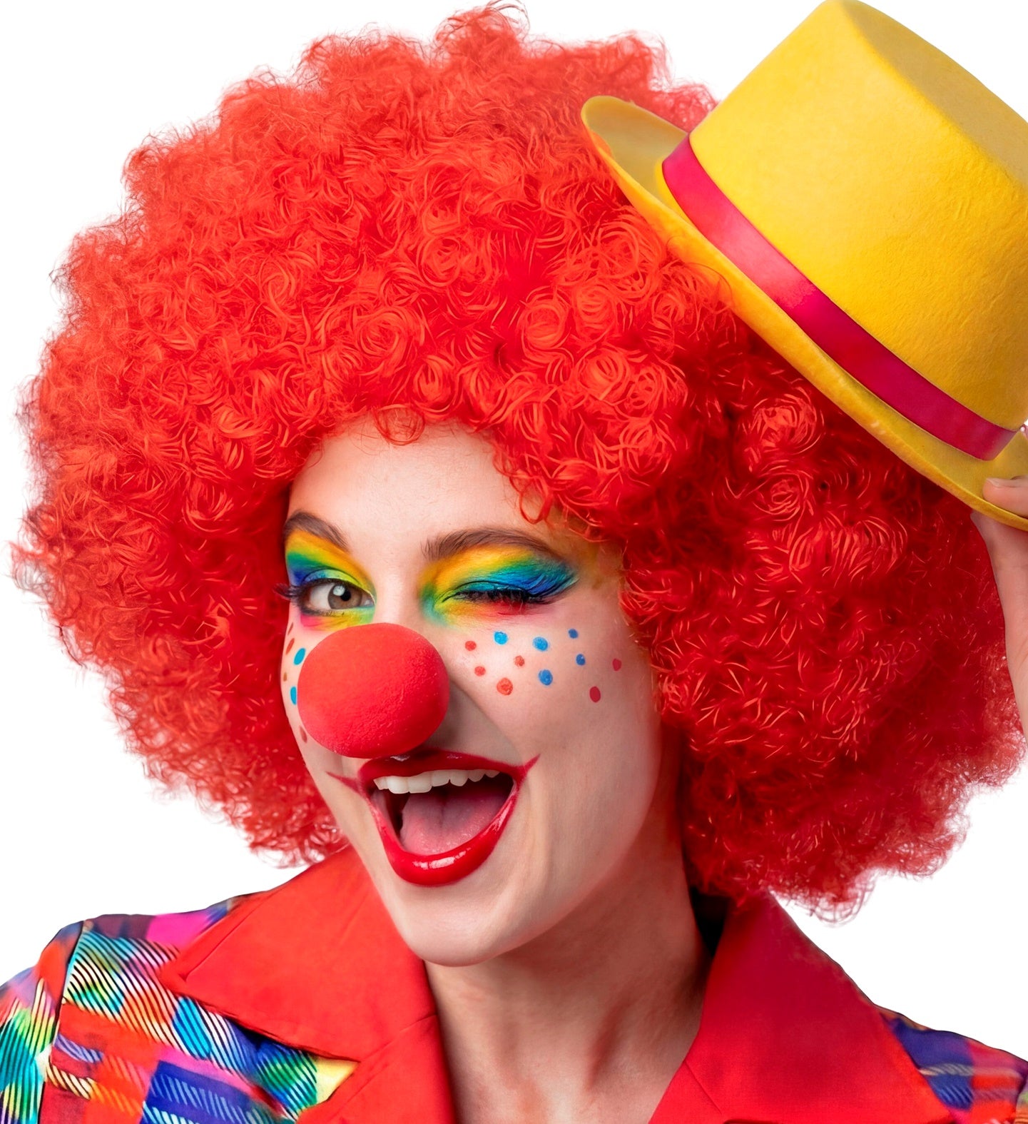 A smiling clown wearing a vibrant red curly wig, a small yellow top hat, colorful rainbow eye makeup, and a bright red sponge clown nose.
