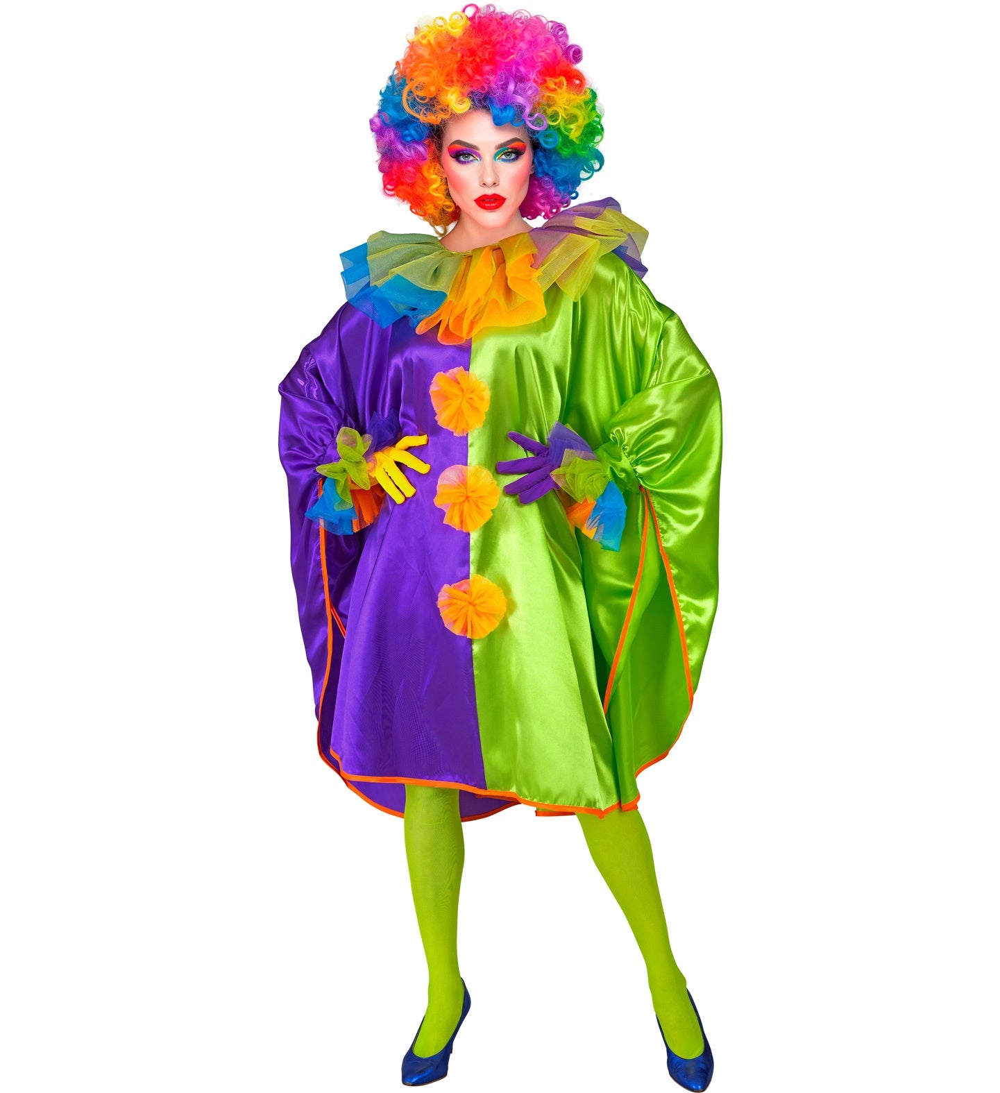 A woman wearing a large rainbow afro wig poses in a colorful purple and green clown poncho with orange pom-poms.
