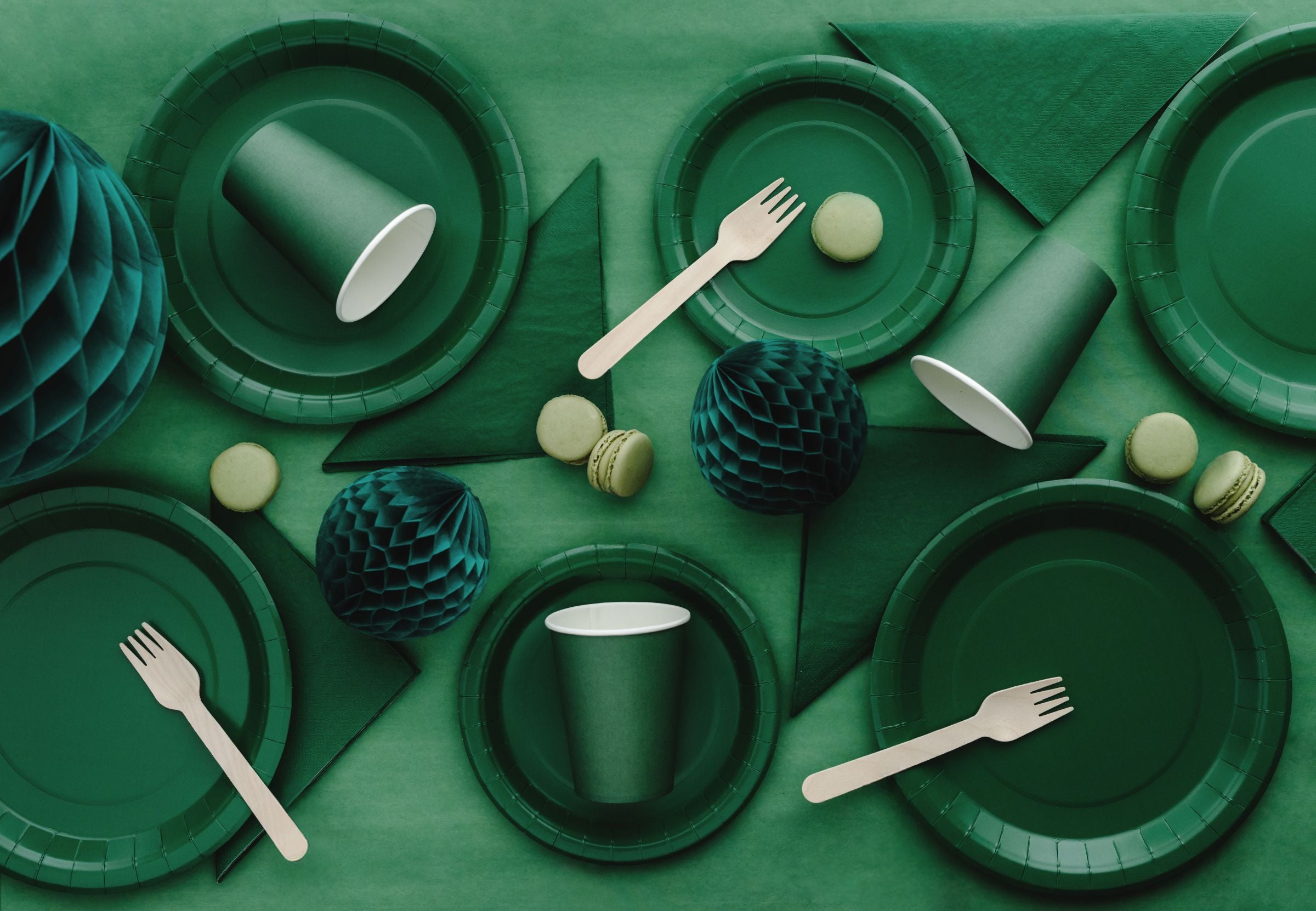 A flat lay of dark green party supplies (plates, cups, napkins) clustered with other decor.