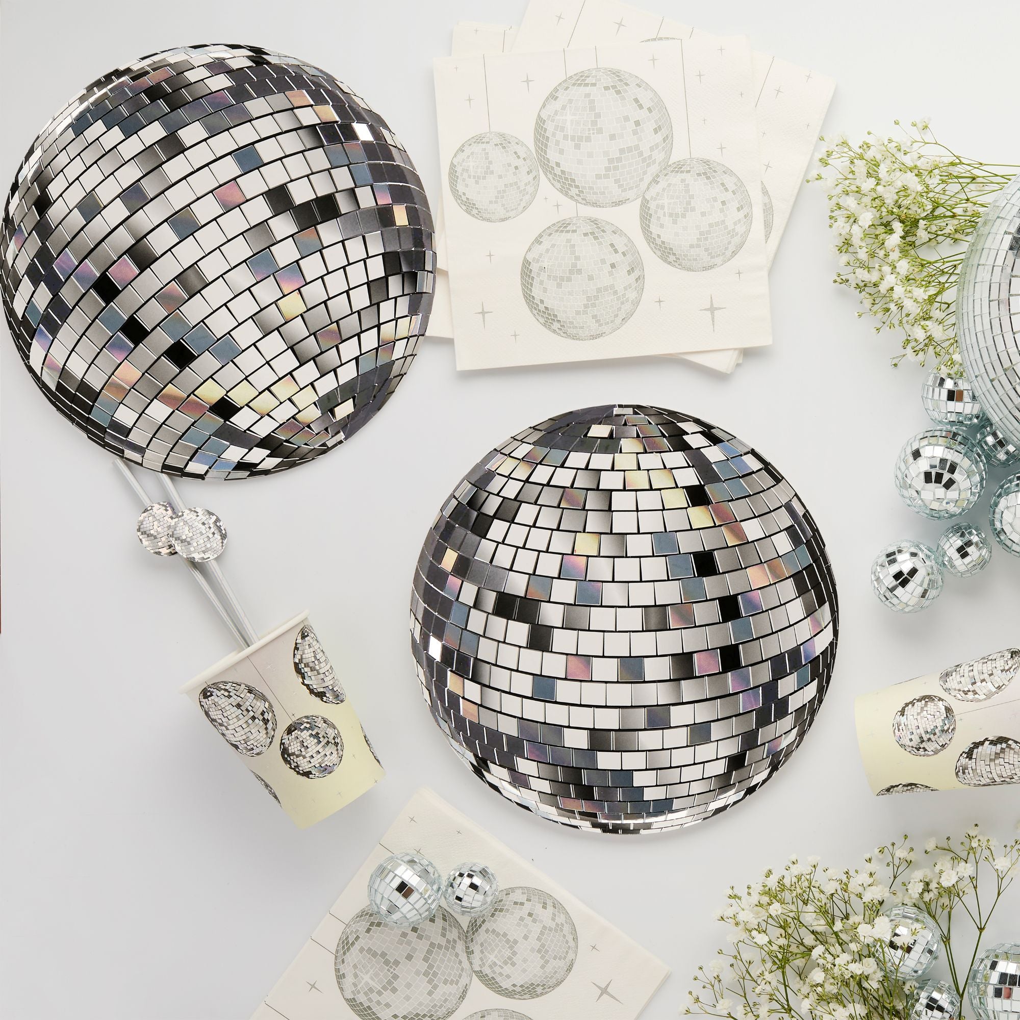 Disco ball paper plates arranged on a white table surrounded by matching cups, napkins, and baby's breath flowers.