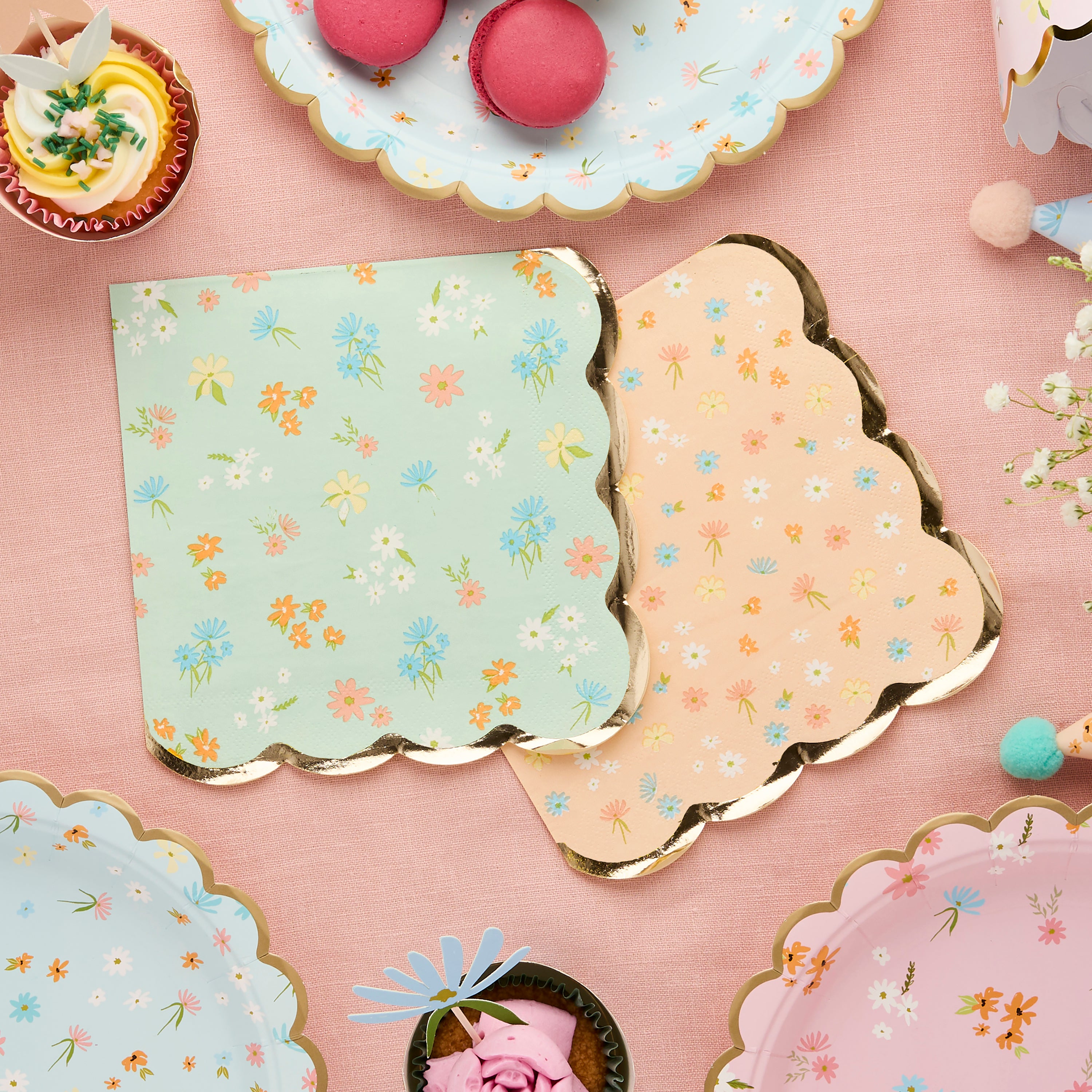 Floral scalloped napkins arranged on a pink tablecloth with matching wildflower plates and party treats.