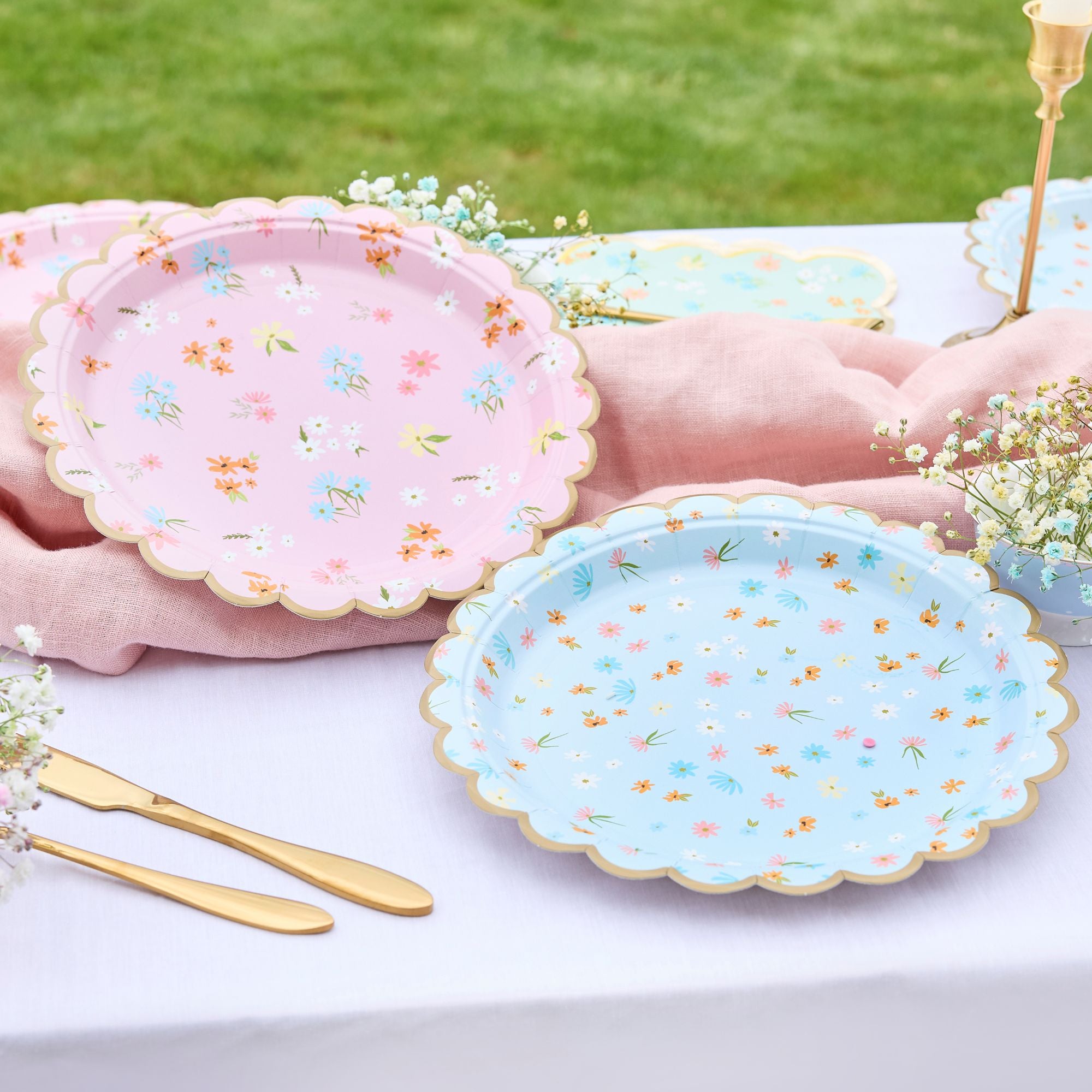 Pastel floral paper plates arranged on a white tablecloth with gold cutlery for a garden party.