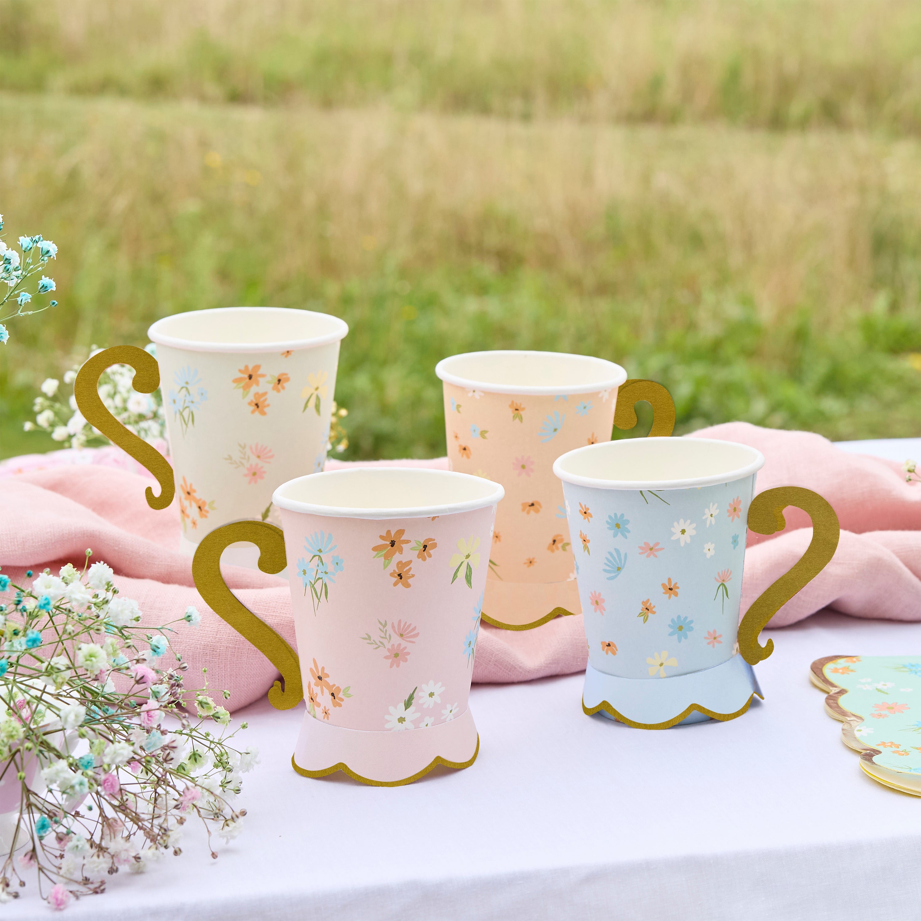 Pastel floral tea party cups arranged on a white tablecloth with matching wildflower plates and spring flowers.