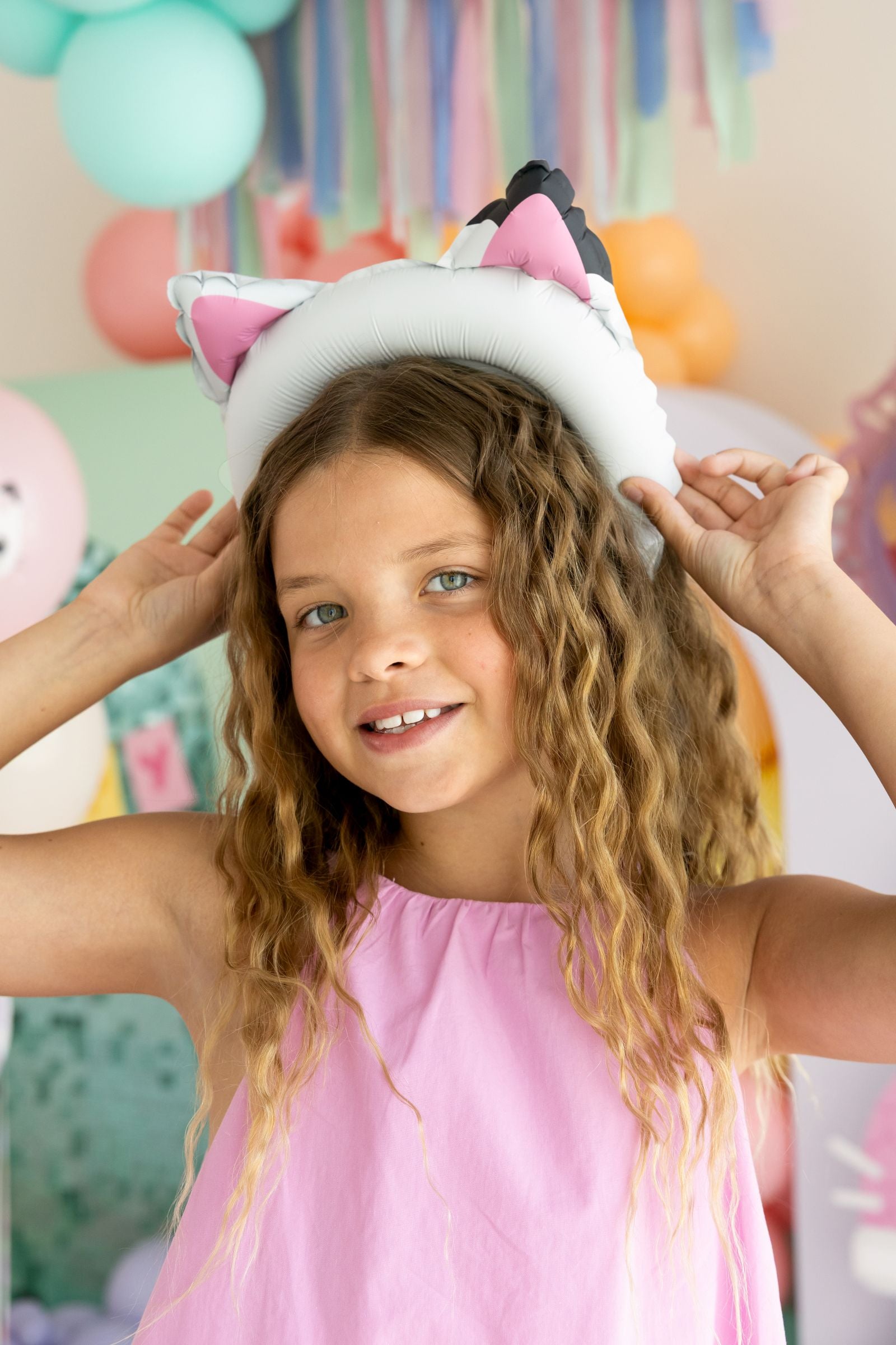 A smiling child wearing an inflated Gabby cat ear foil headband at a colorful birthday party.