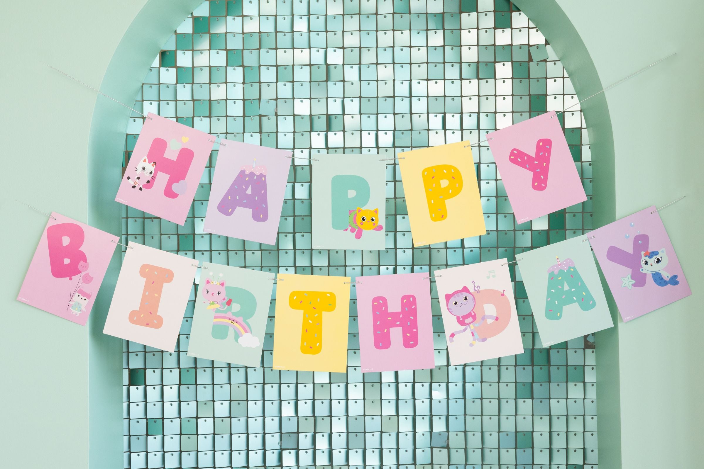 Colorful Gabby’s Dollhouse Happy Birthday cardstock bunting banner hanging on a teal shimmer wall.