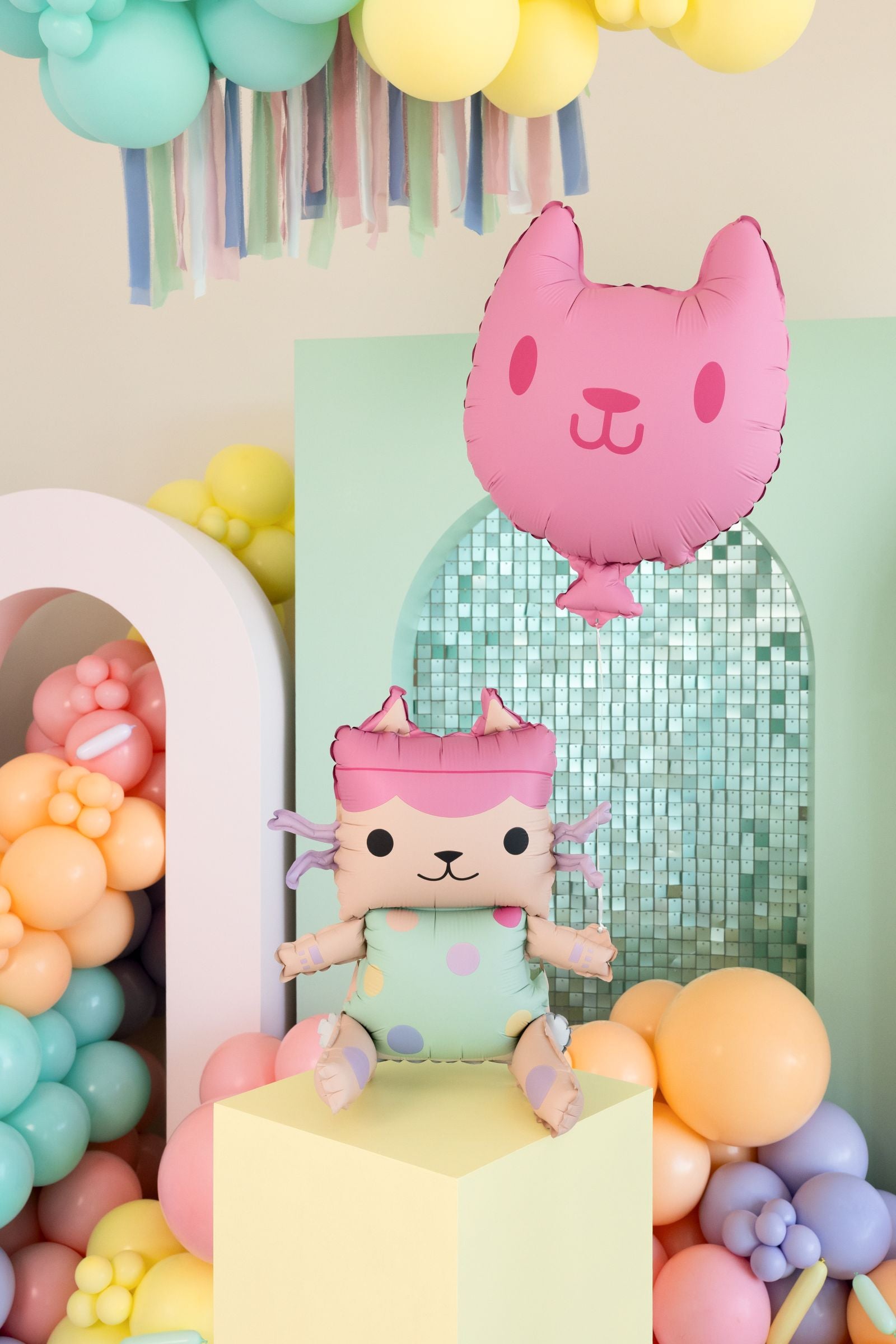 A standing Baby Box foil balloon next to a floating pink cat balloon against a colourful party backdrop.