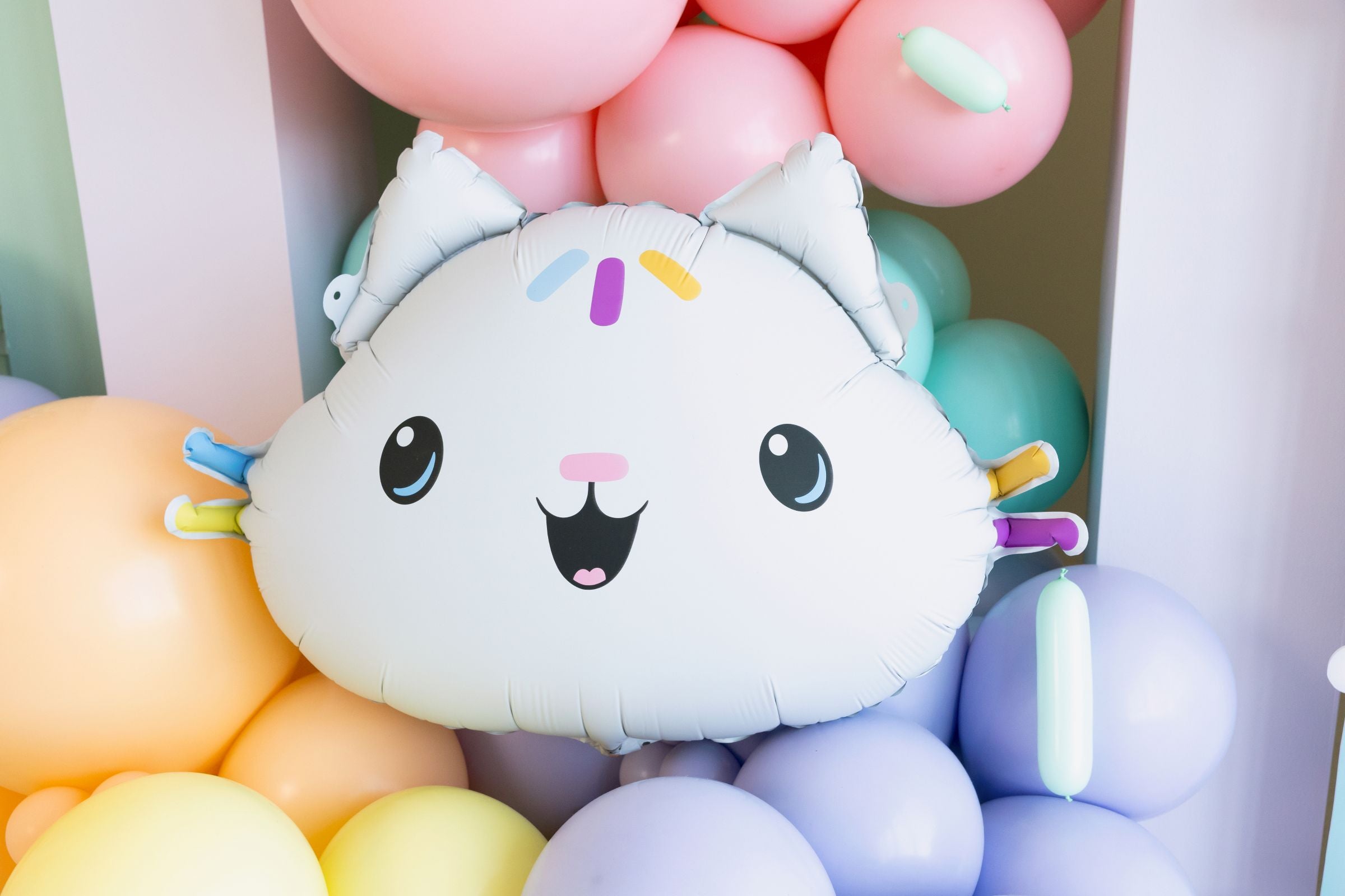 Giant Cakey Cat shaped foil balloon with white finish and colorful sprinkle details,  surrounded by pastel balloons.