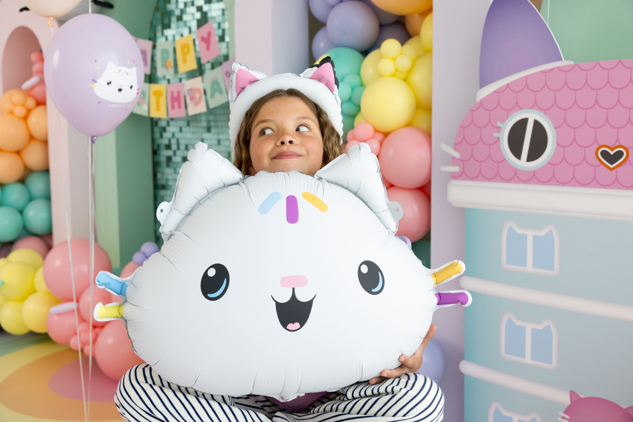 A child playfully holding a large Cakey Cat foil balloon at a Gabby's Dollhouse themed birthday party.