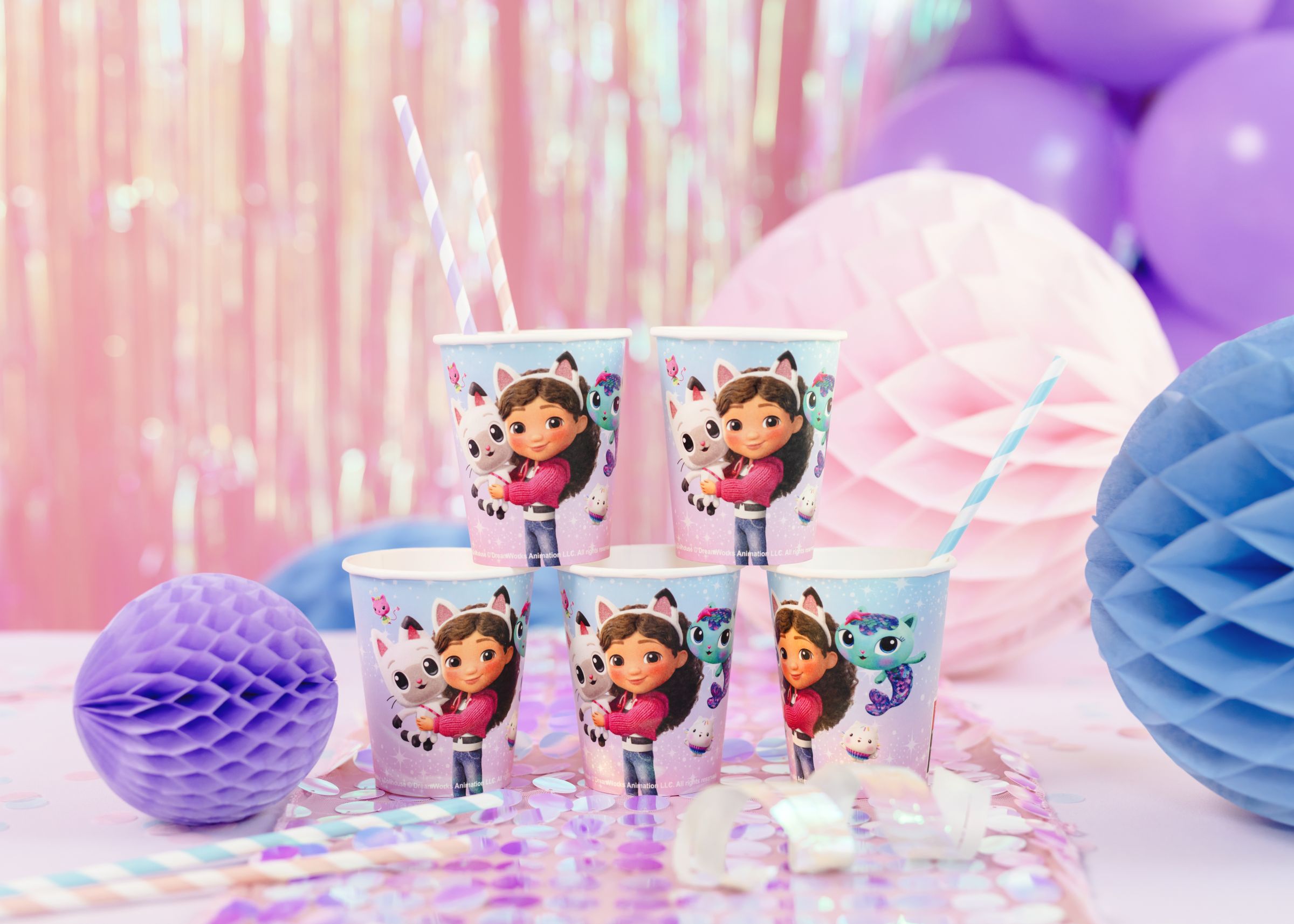 A stack of Gabby's Dollhouse movie paper cups arranged with blue and pink striped straws on a party table.
