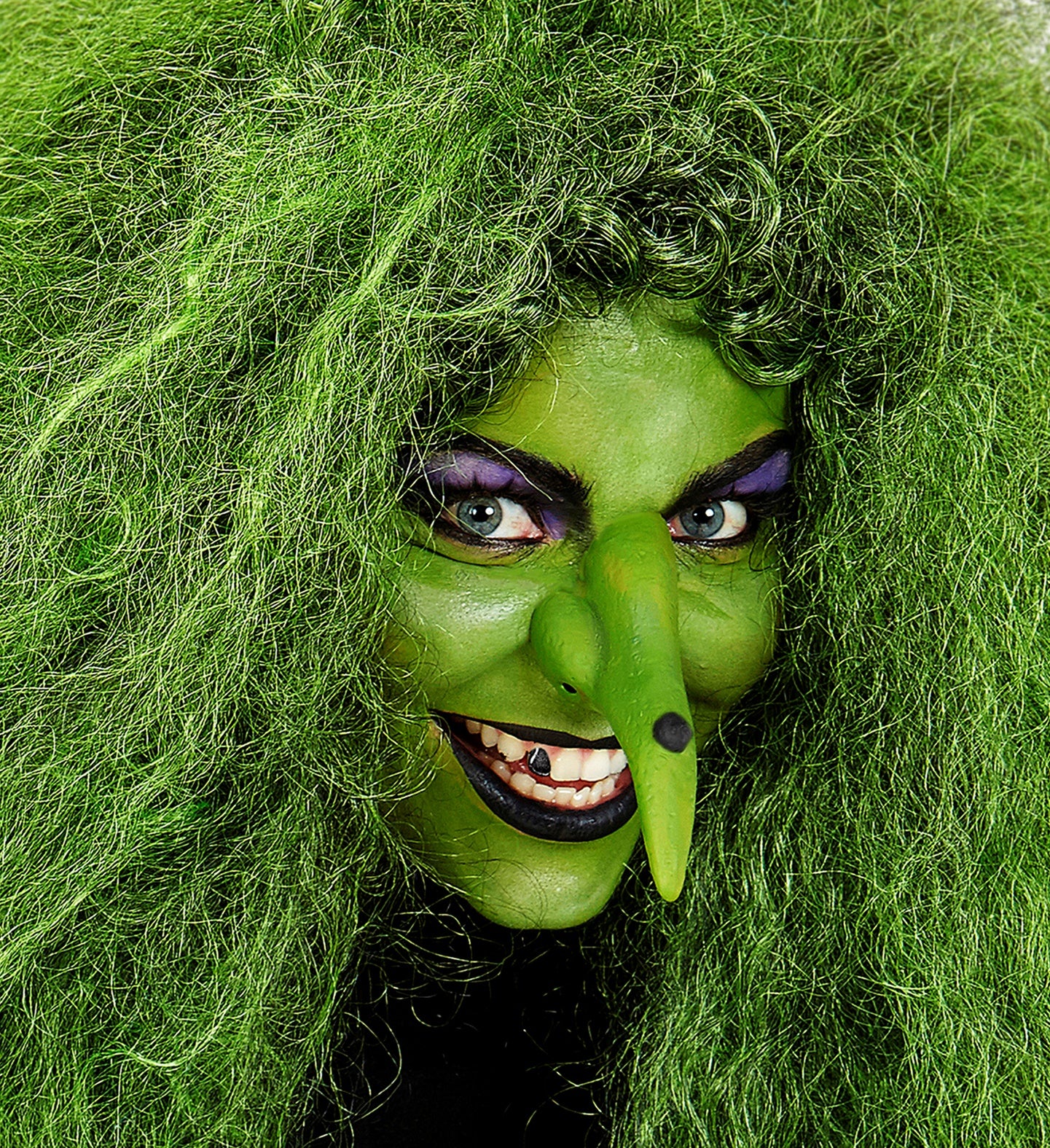 A woman in a wicked witch costume using the green face paint, a prosthetic nose, and a large green wig.