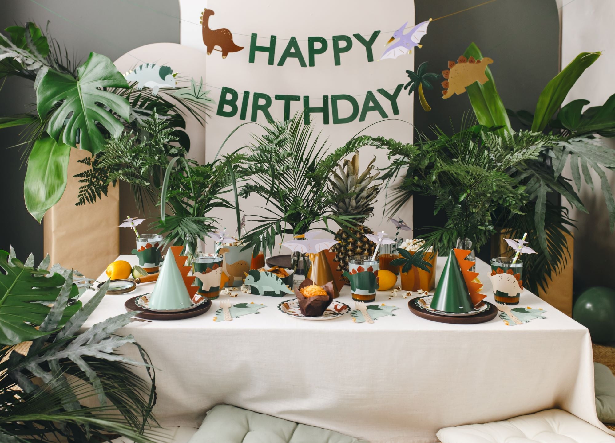Birthday party setup with dinosaur-themed decorations, including a 'Happy Birthday' banner and green party hats.