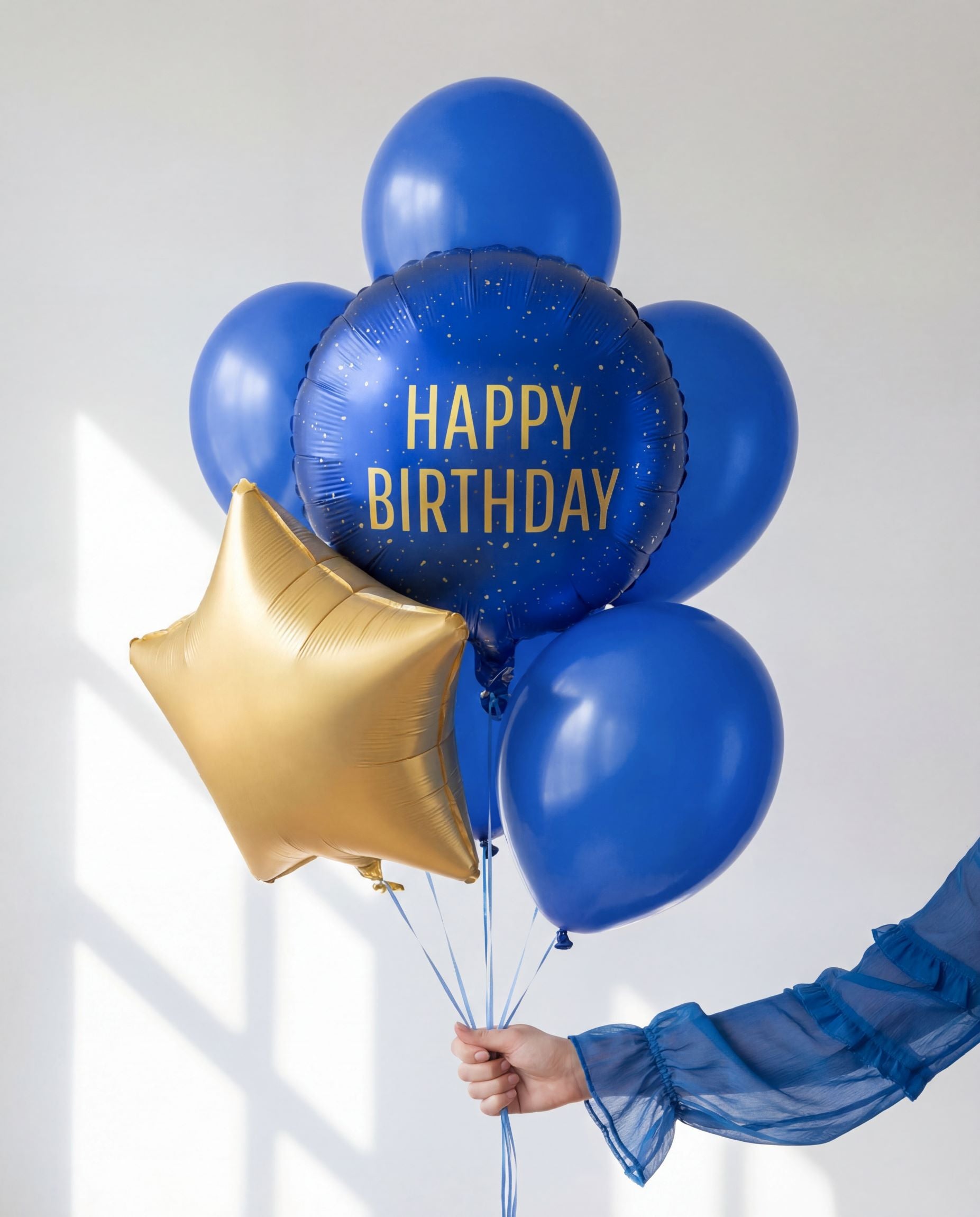 Hand holding a bouquet of balloons including the navy blue Happy Birthday foil, a gold star, and matching blue latex balloons.