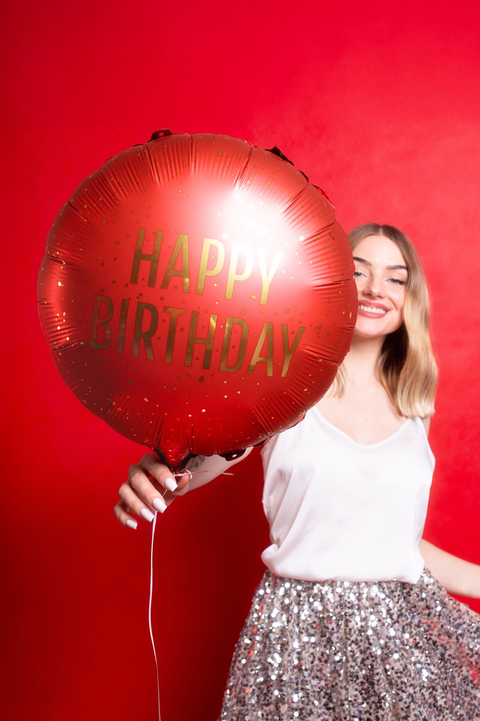 Person holding a large dark red Happy Birthday foil balloon against a matching red background.