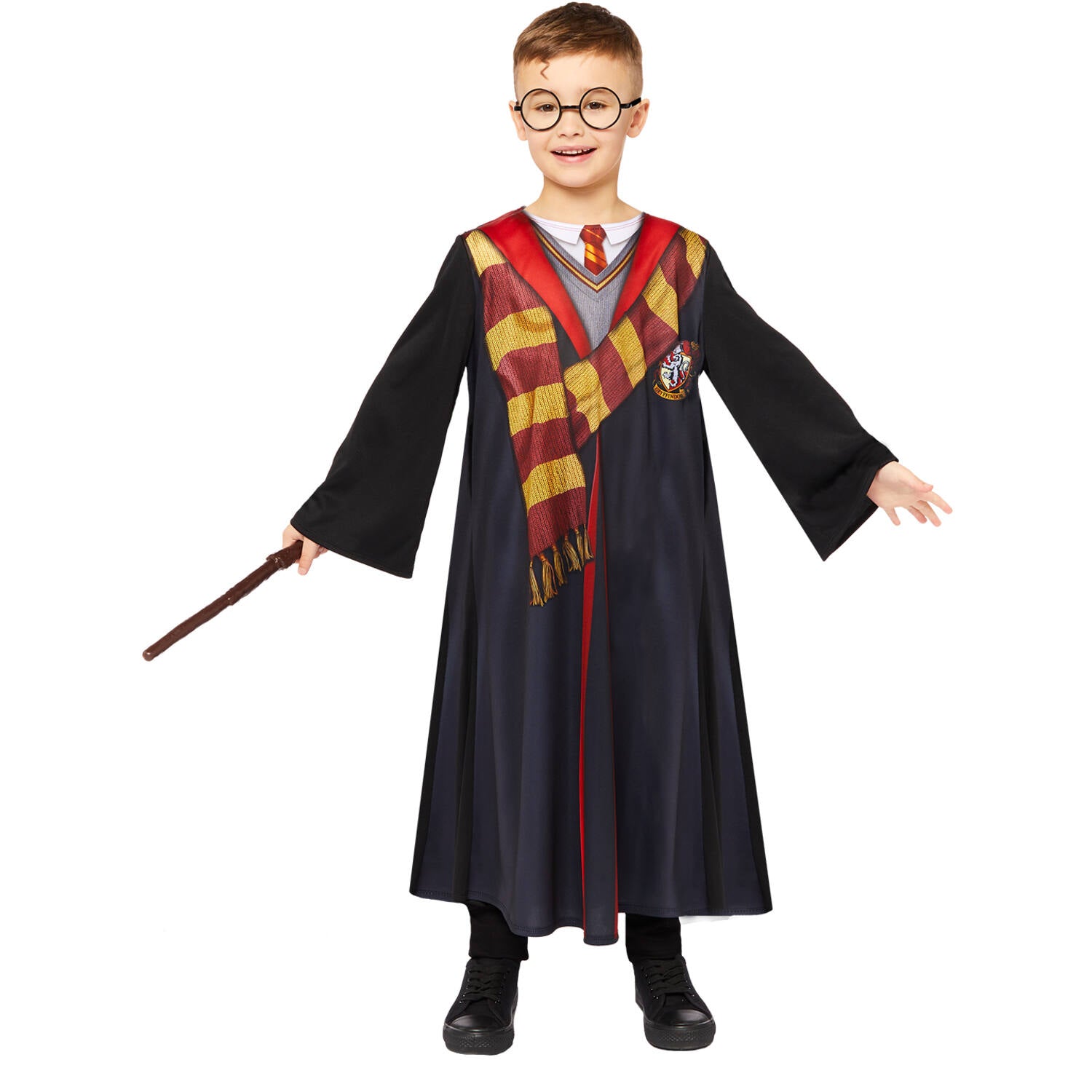 A child standing forward modeling an official licensed Harry Potter costume robe featuring a printed Gryffindor tie and scarf, holding a plastic toy wand and wearing round black glasses.