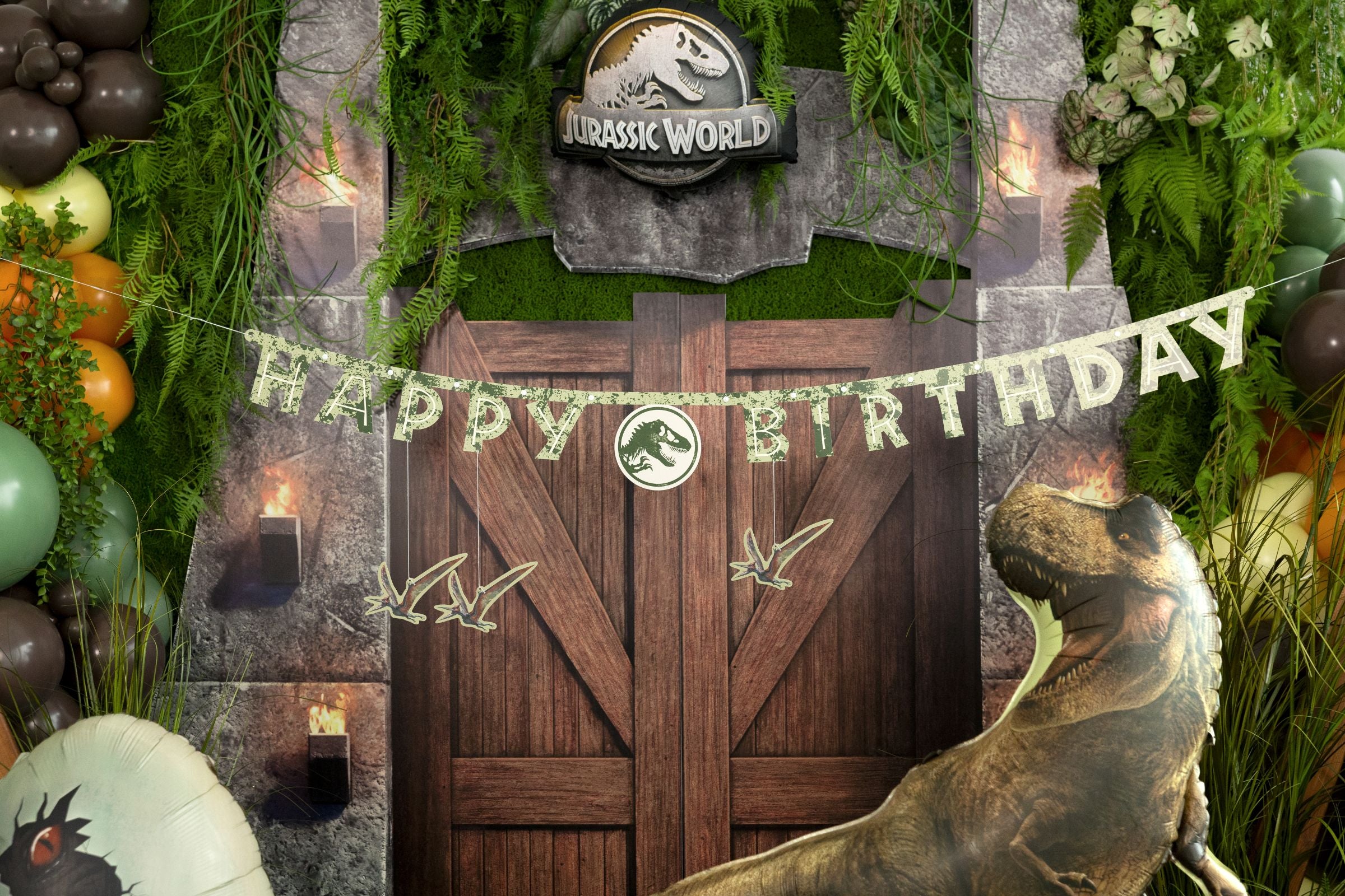Jurassic World Happy Birthday paper banner displayed across a jungle-themed party gate with a large T-Rex balloon and tropical greenery.