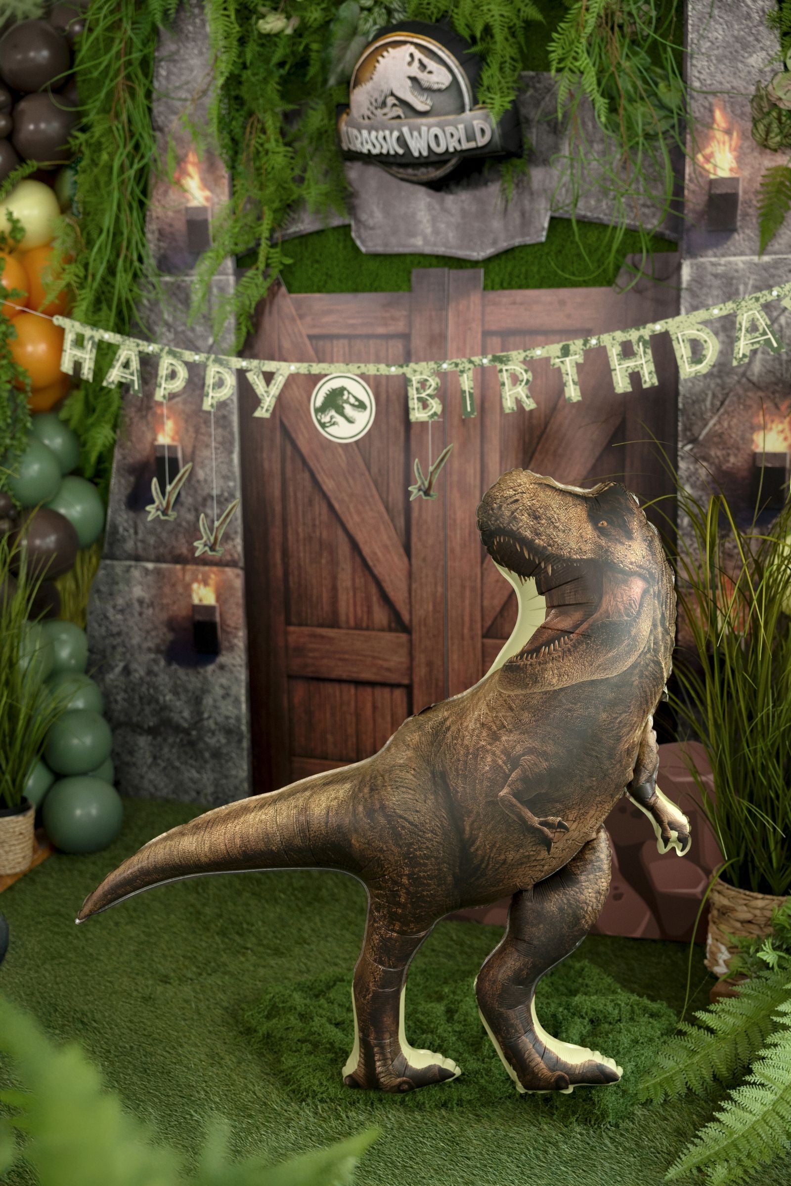 Large realistic brown T-Rex foil balloon standing in front of a Jurassic World themed birthday gate backdrop.