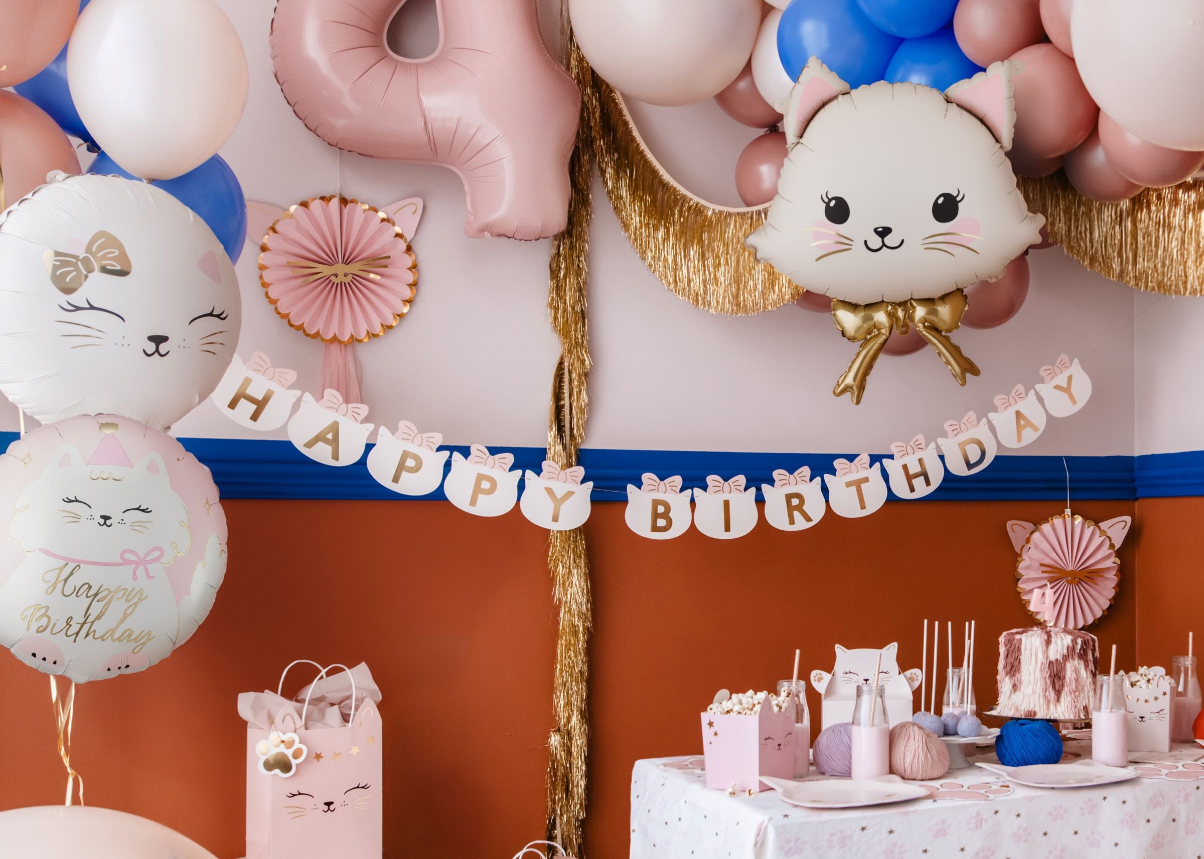 Festive cat-themed birthday party setup with kitty foil balloons, a cat-shaped banner, and matching tableware.