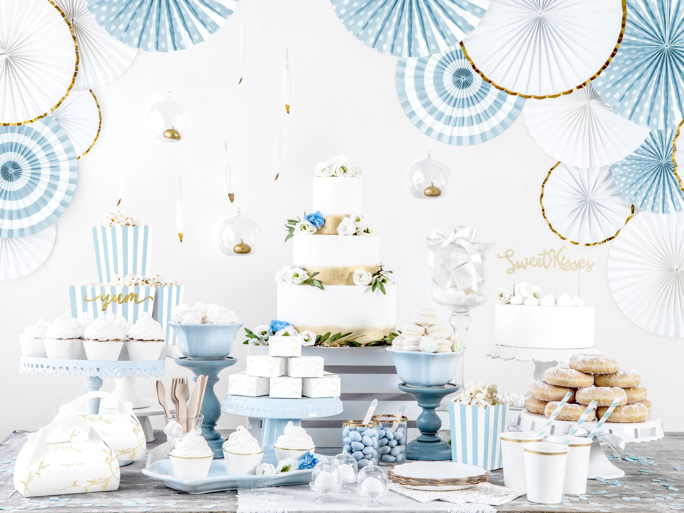 An elegant blue and white dessert table featuring striped straws, blue fans, and gold-rimmed plates.