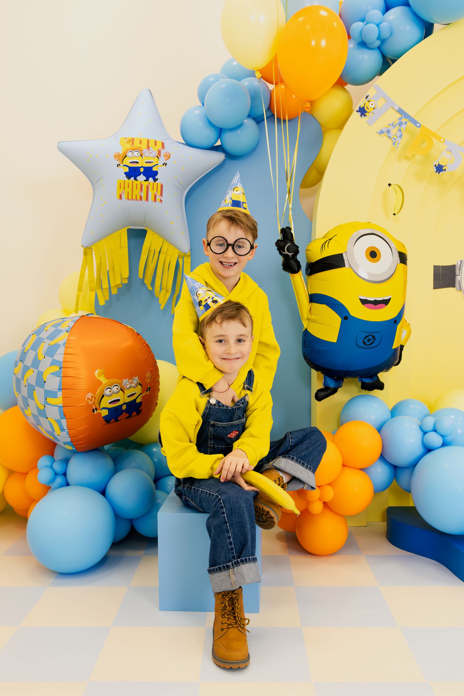 Minion Mel foil balloon displayed with two children in Minion costumes at a fully decorated birthday party.