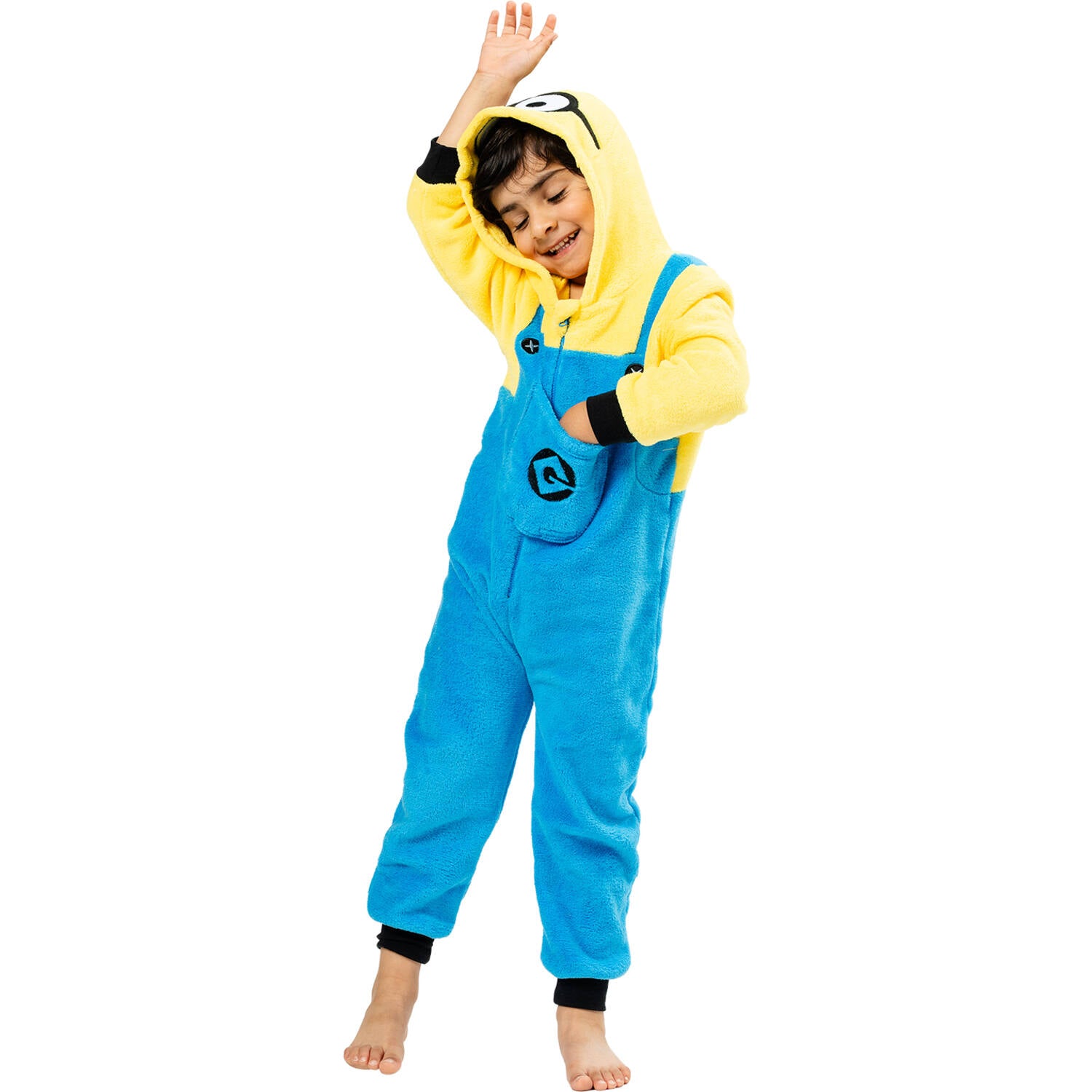 A happy child smiling and posing playfully with one hand raised, wearing a cozy plush Minions character jumpsuit with a front pocket.
