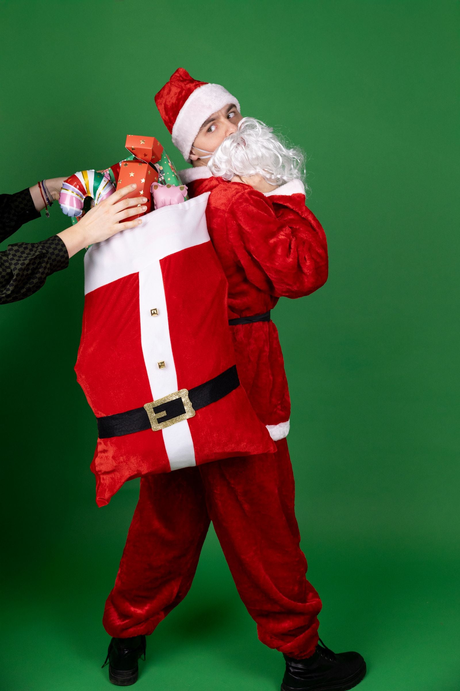 A person in a Santa Claus costume carrying the large red gift sack over their shoulder as a prop.