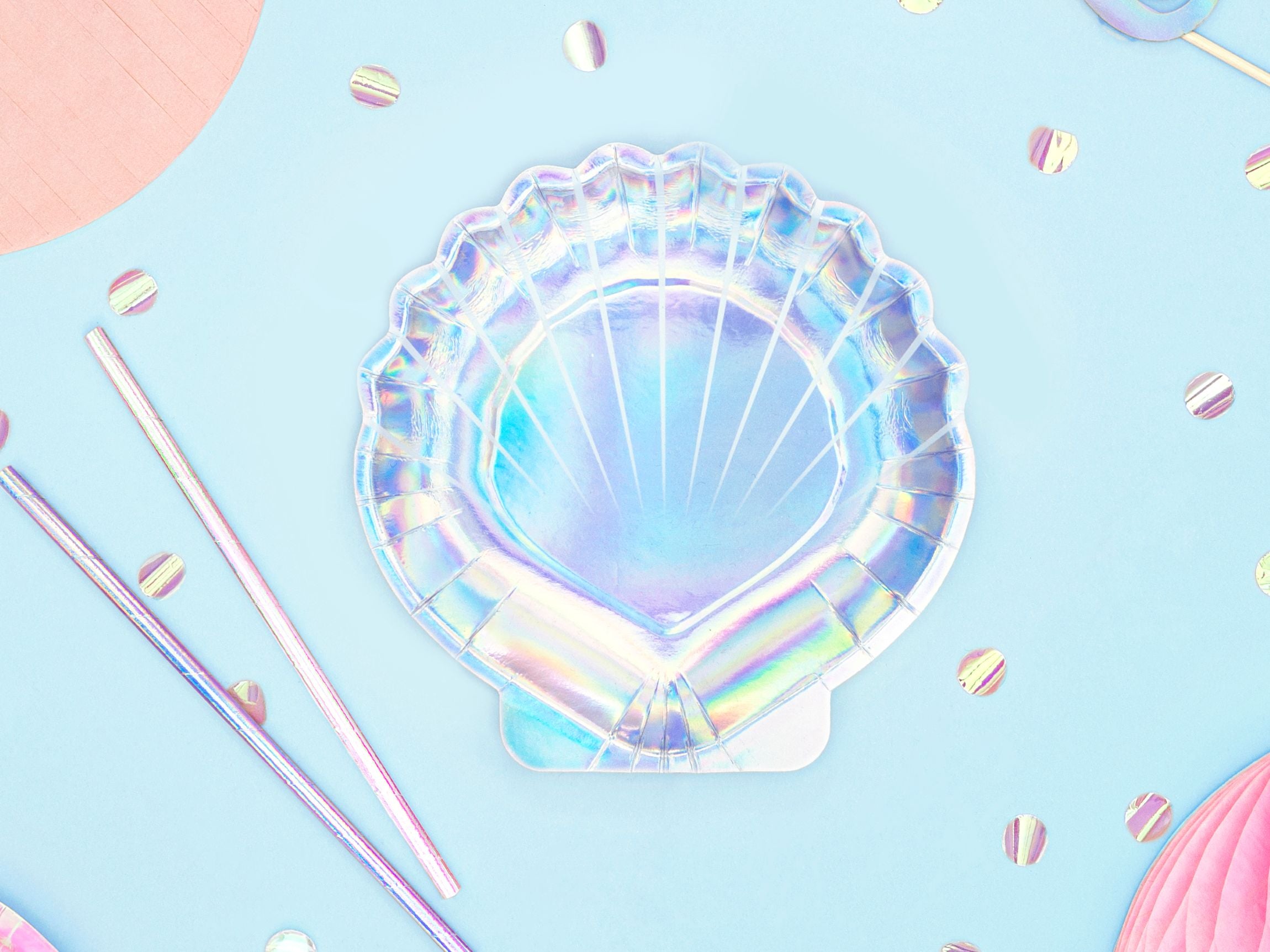 An overhead view of a single iridescent seashell-shaped paper plate, shimmering with various colors, centered on a light blue background with scattered iridescent confetti and pink and silver striped straws.