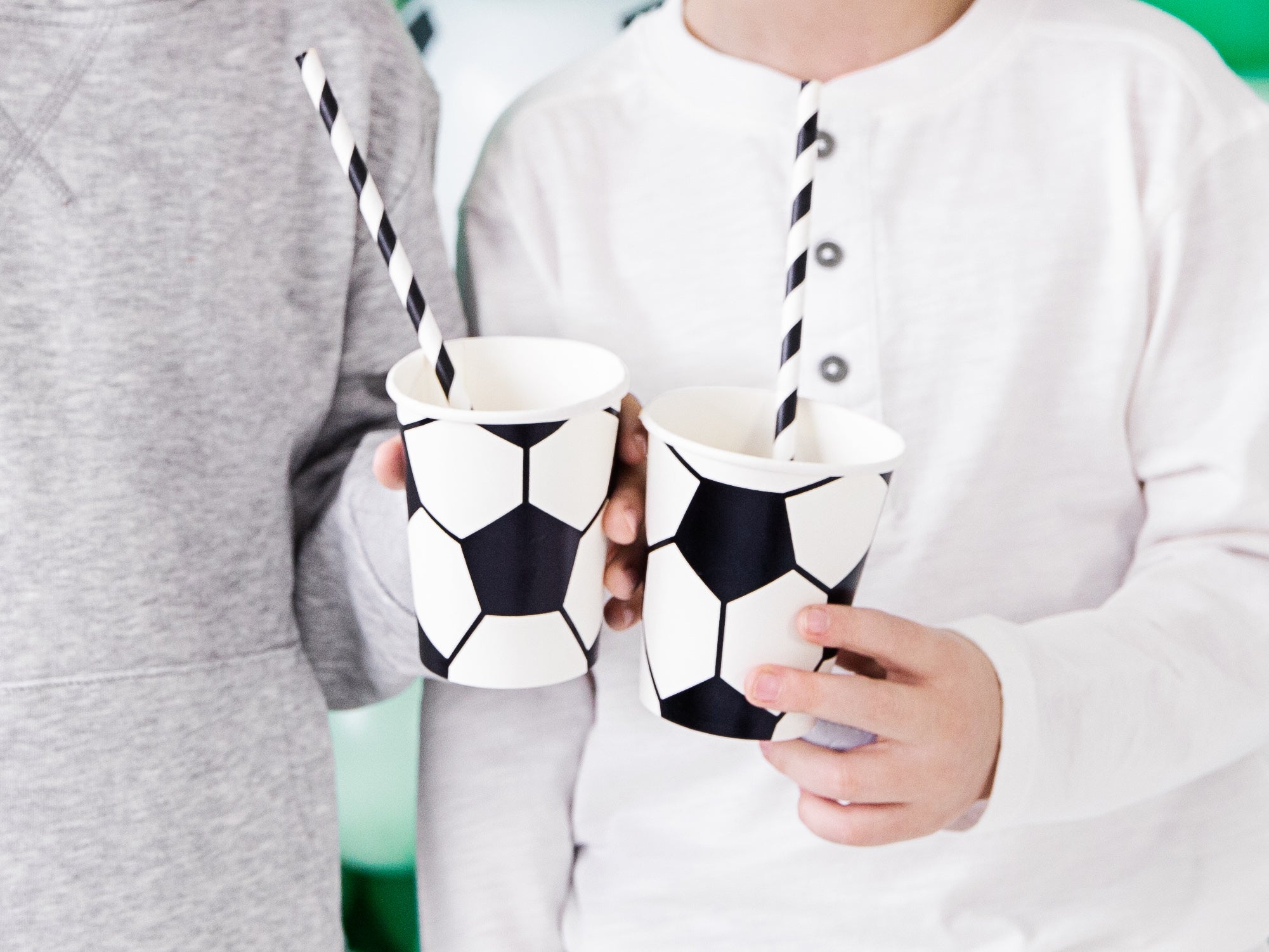 Two people holding black and white soccer ball patterned paper cups with striped straws, focusing on their hands and the cups.