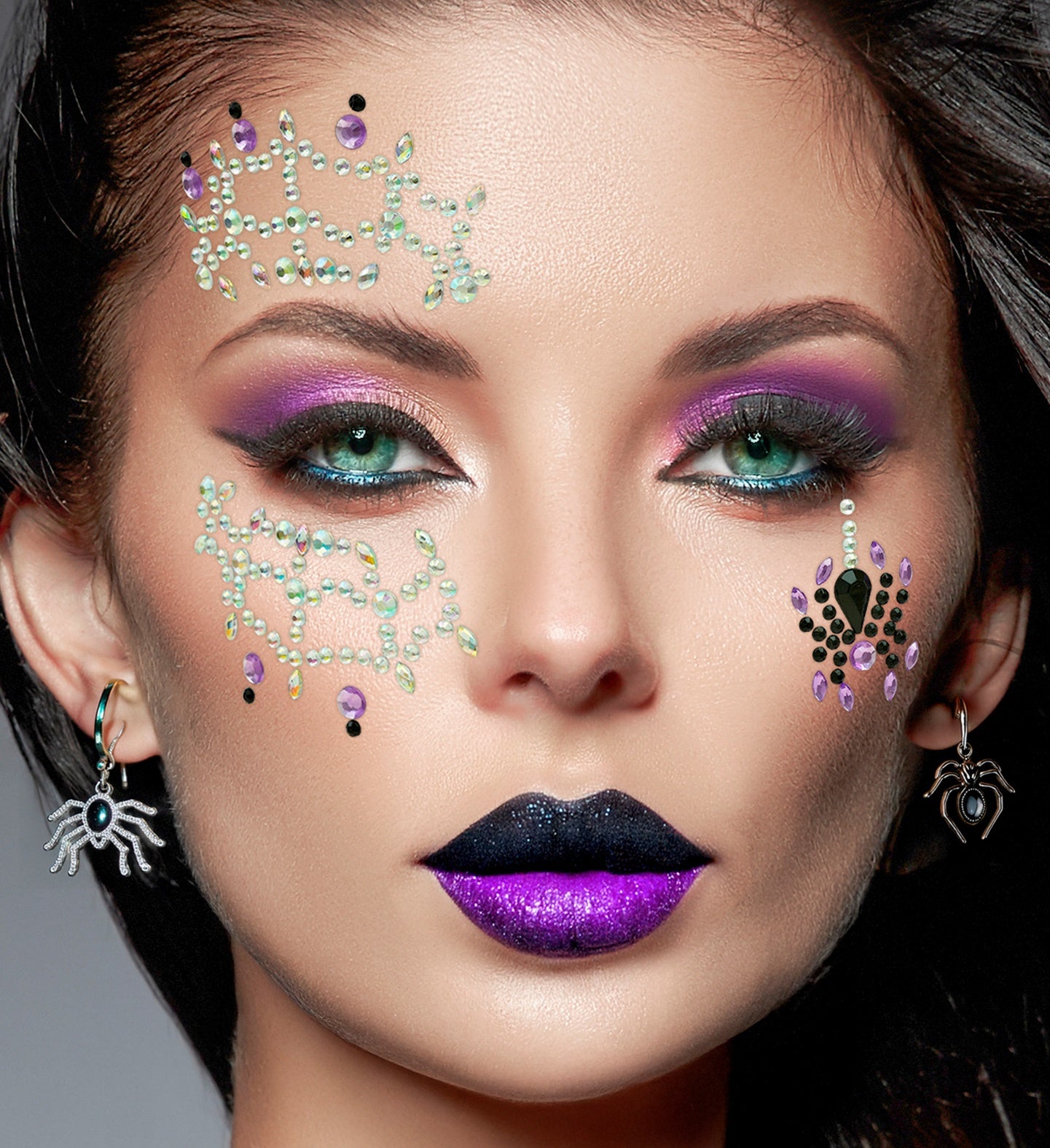 A person wearing dramatic purple and black makeup, spider earrings, and iridescent spiderweb face jewels with a jeweled spider accent.