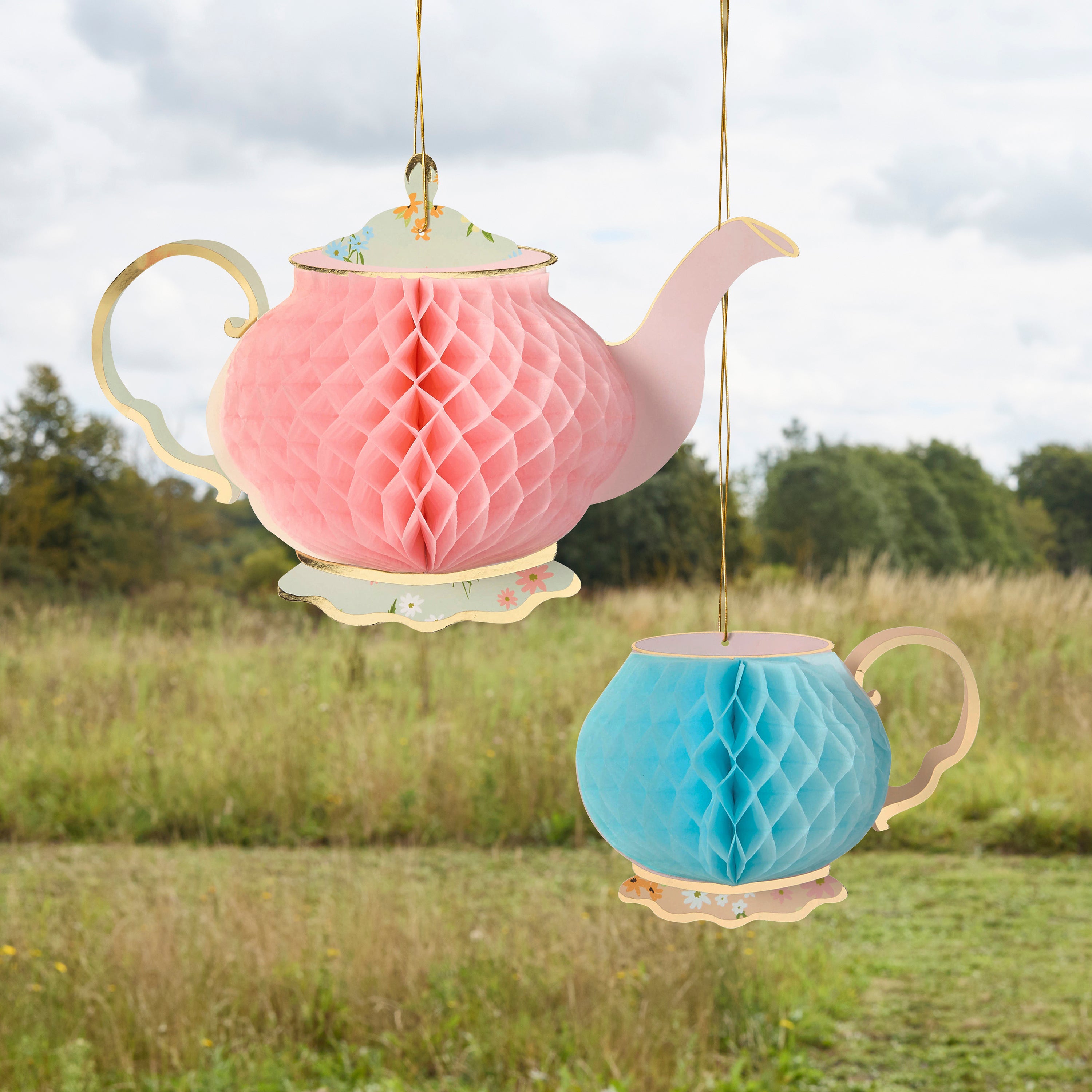 3D teapot and teacup honeycomb decorations hanging from a tree in a sunny garden party setting.