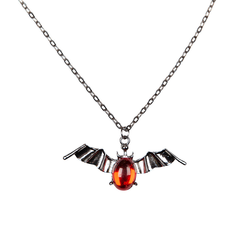 A silver-tone necklace with a pendant shaped like bat wings holding a central, oval, faceted red gem.
