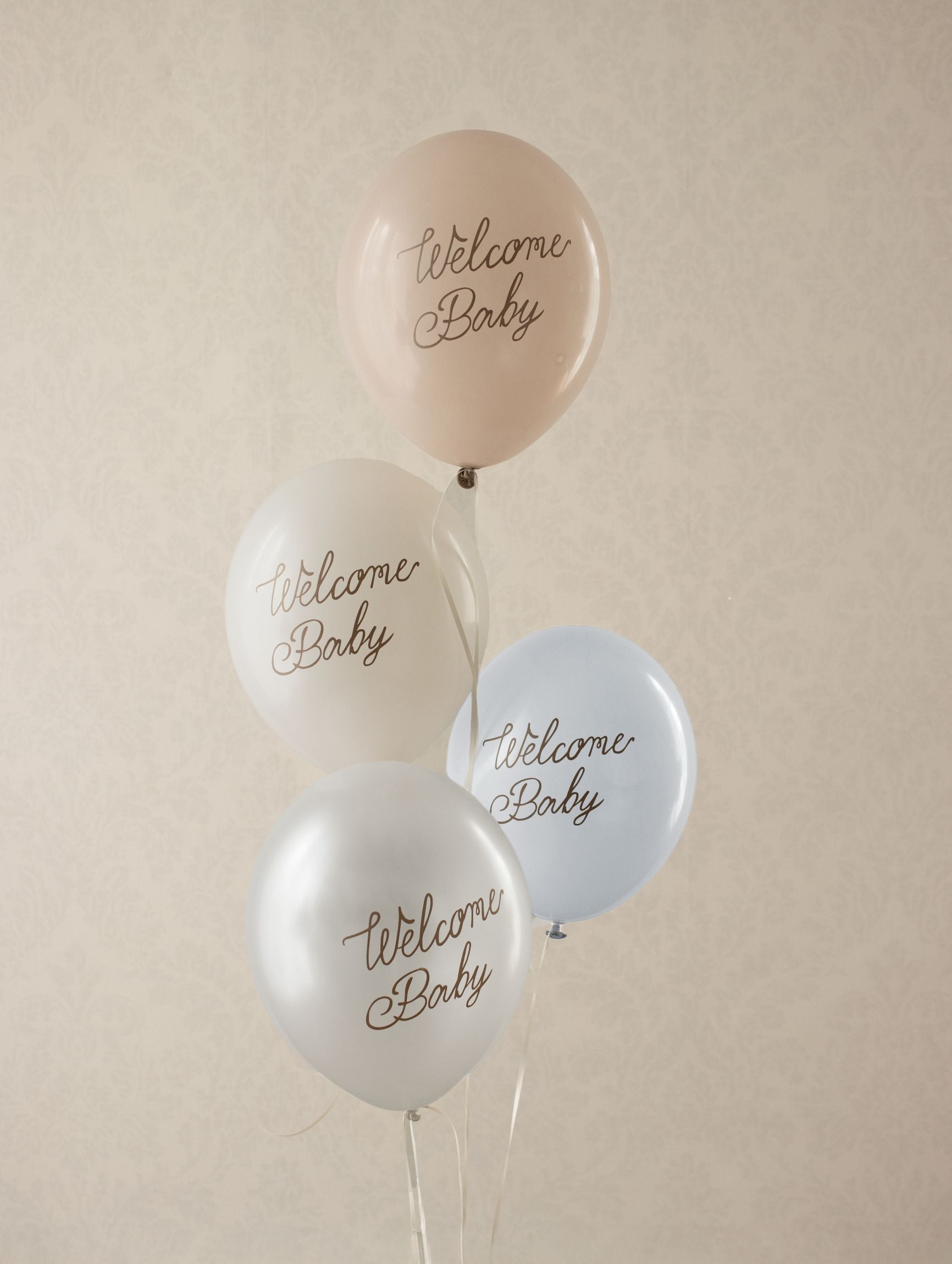 A cluster of four Welcome Baby balloons in pastel tones floating in a decorated room.