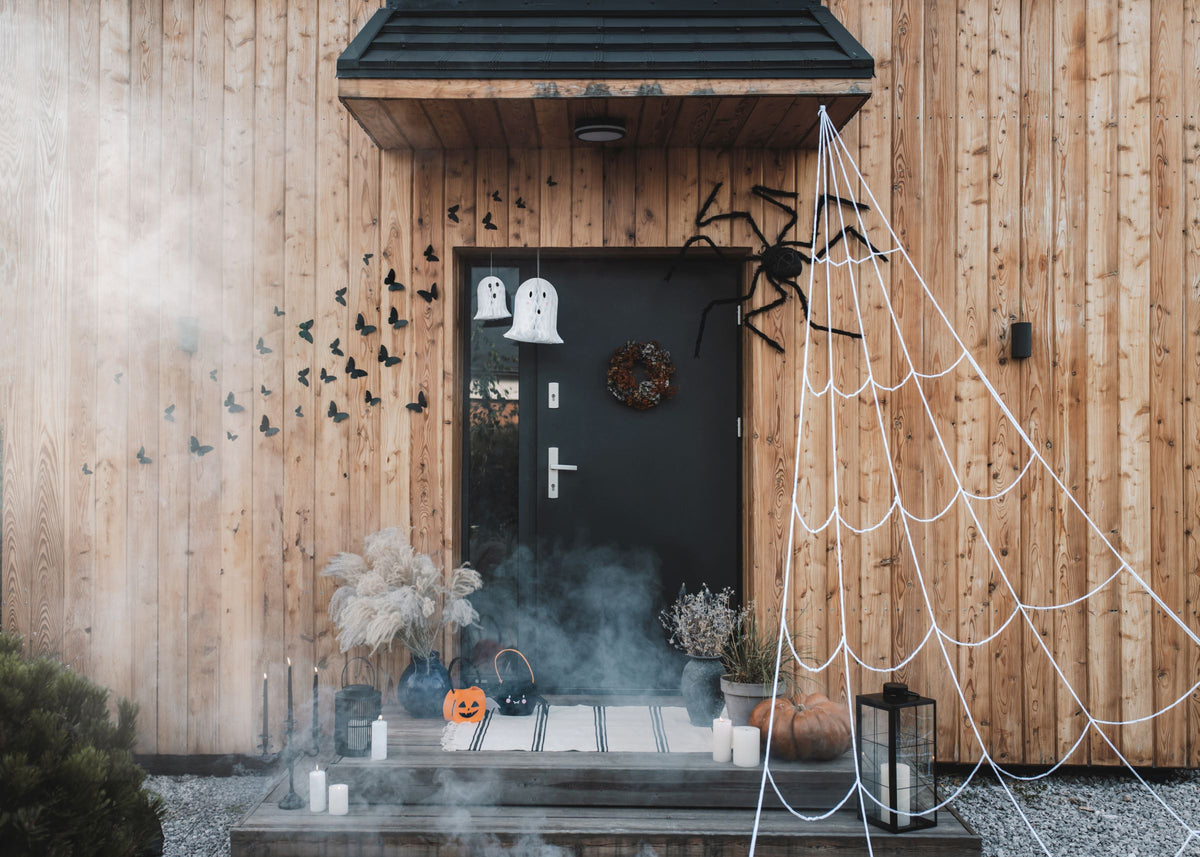 Large white spider web decoration draped across a residential doorway on a wooden exterior with spiders and ghosts.