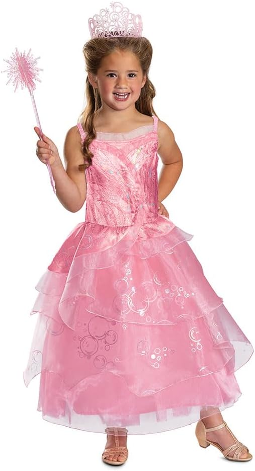 A smiling girl models the official Wicked Glinda costume, which includes a beautiful pink layered dress with a bubble print, and is holding a prop wand.