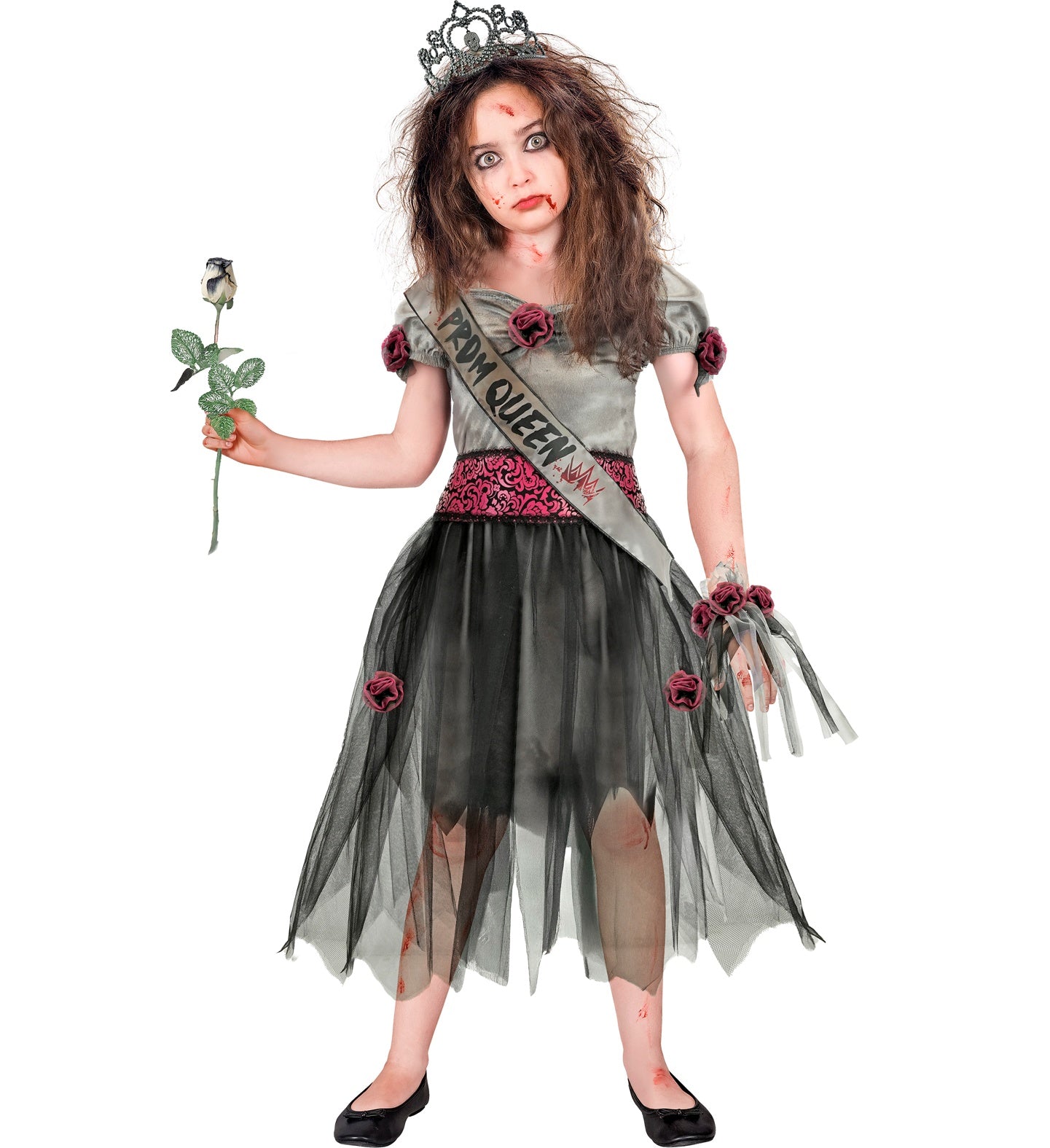 A young girl with backcombed messy hair and zombie special effects face paint looking seriously at the camera in a tattered zombie prom queen dress while holding a dark rose prop.