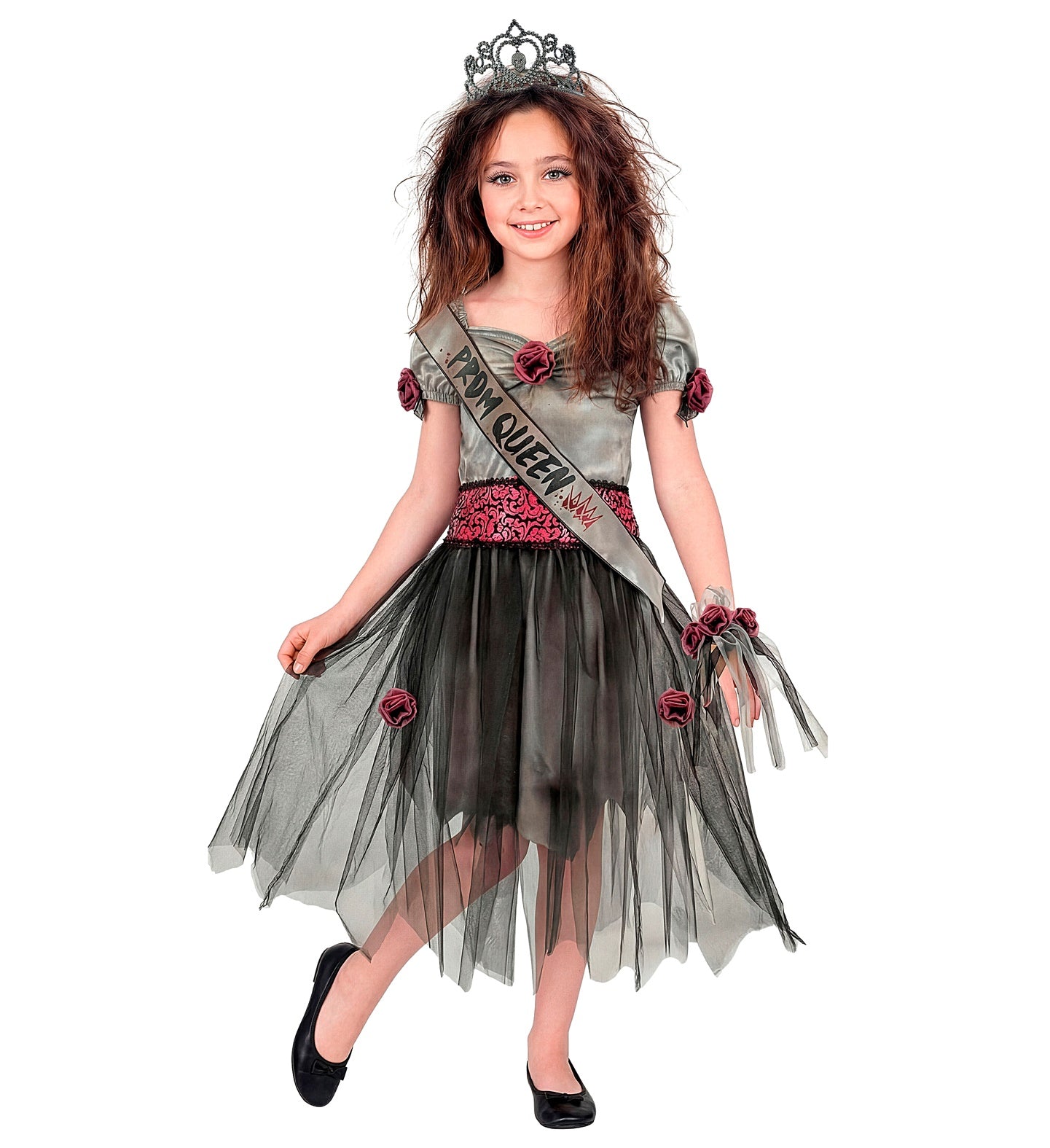 A young girl with long wavy hair smiling in a zombie prom queen Halloween costume, featuring a grey dress with black tulle, a pink damask belt, a prom queen sash, and a dark tiara.