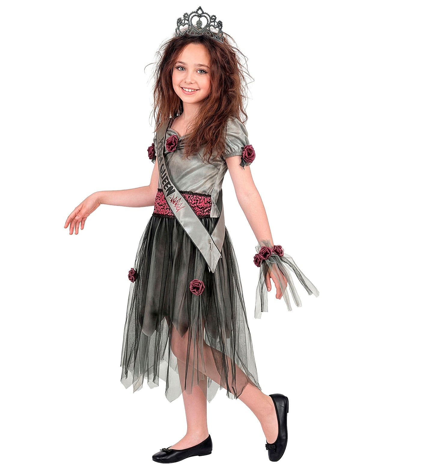 A side-angle view of a young girl posing playfully in a tattered zombie prom queen dress, showcasing the full outfit layer of black tulle over grey fabric, a patterned waist sash, and a wrist corsage.
