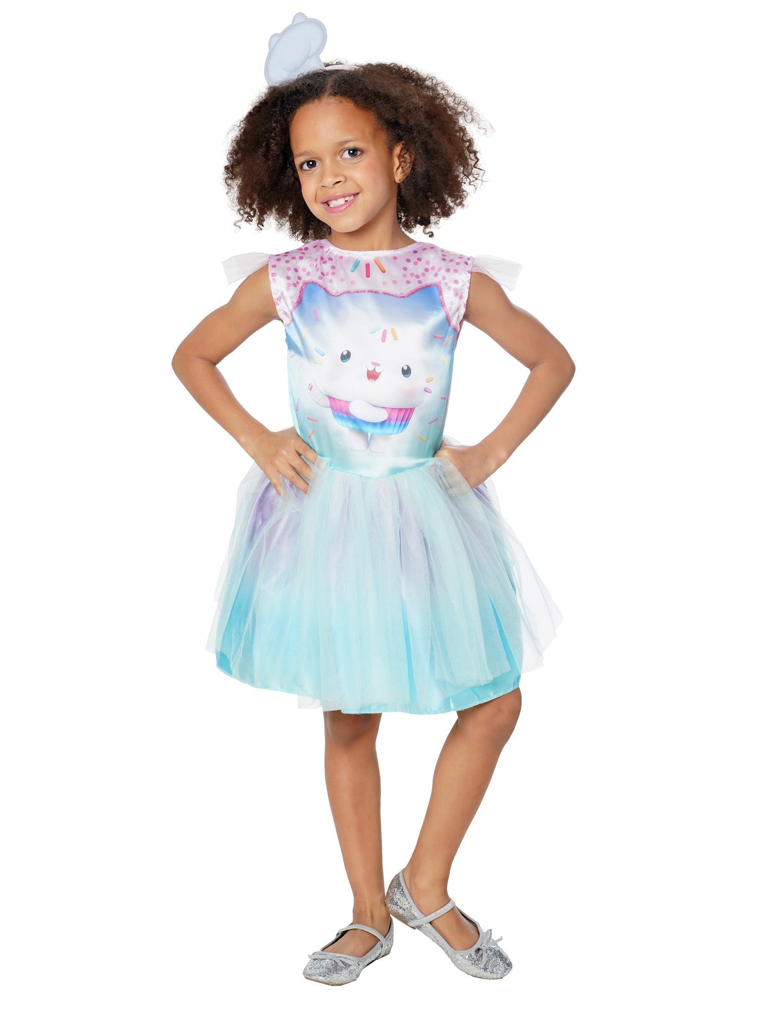 A smiling young girl modeling a pastel Gabby's Dollhouse Cakey Cat fancy dress costume, featuring a sprinkle-printed bodice of Cakey Cat with sheer flutter sleeves, an ombre purple and blue tulle tutu skirt, and a matching mini white chef hat headband.