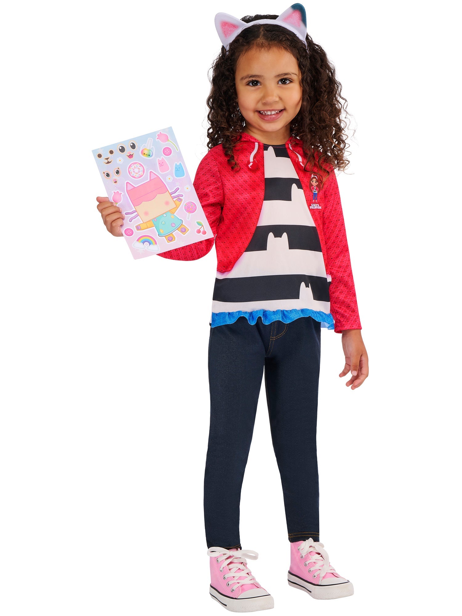 A smiling child wearing a Gabby's Dollhouse outfit and cat-ear headband, proudly holding up the included colorful character sticker sheet.