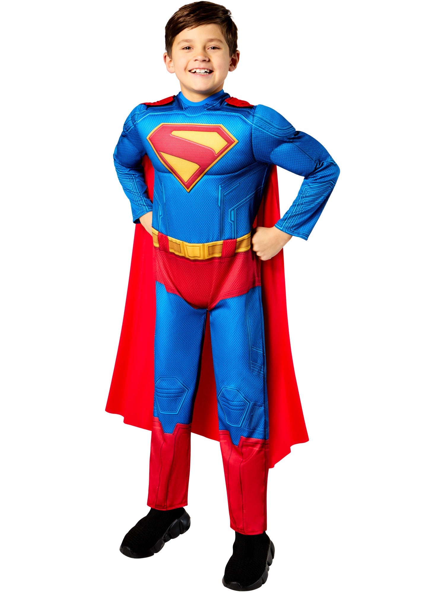 A child smiling, wearing a deluxe Superman costume consisting of a padded blue and red jumpsuit with the iconic "S" emblem, and a flowing red cape.